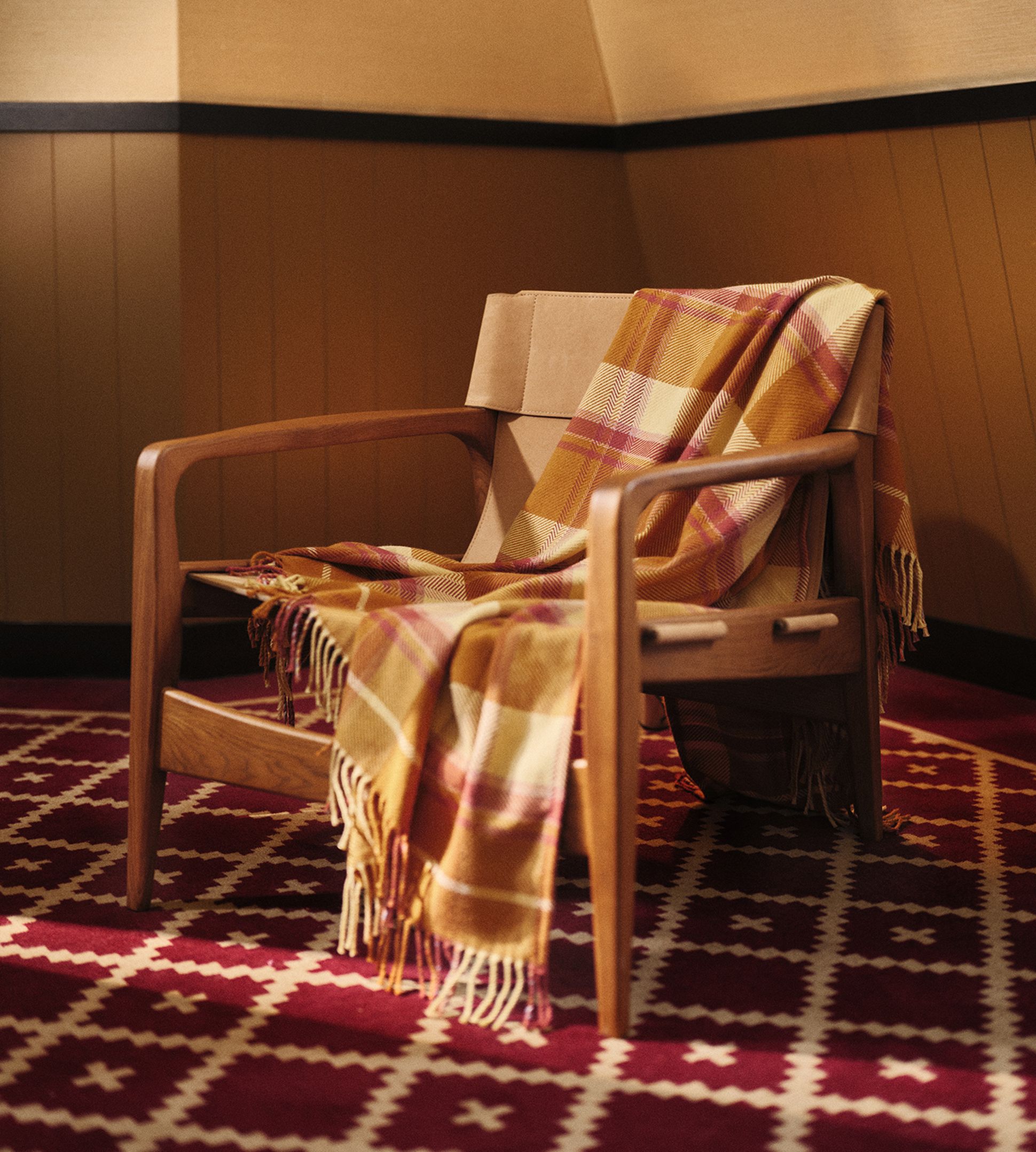 Une chaise en bois recouverte d'une couverture à carreaux aux couleurs chaudes, posée sur un tapis rouge à motifs dans une pièce chaleureuse.
