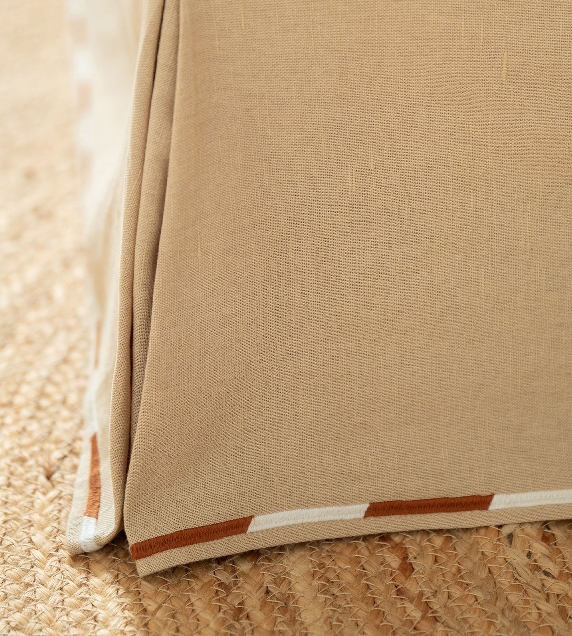 Gros plan sur un coin d'une nappe en tissu beige, bordée de marron et de blanc, drapée sur une surface tissée.