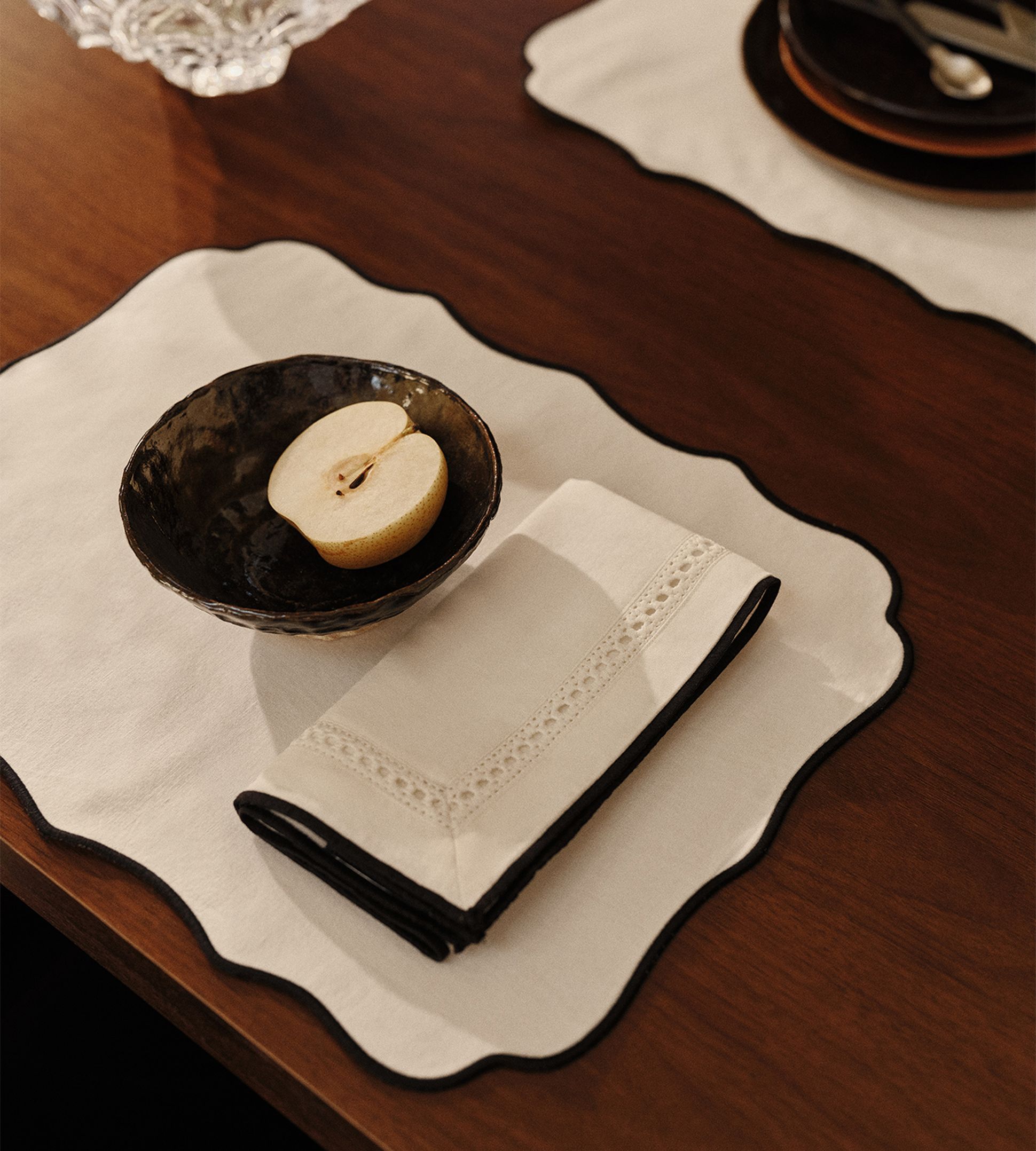 Une pomme coupée en deux repose dans un bol foncé posé sur un set de table festonné, avec une serviette pliée à côté, sur une table en bois.