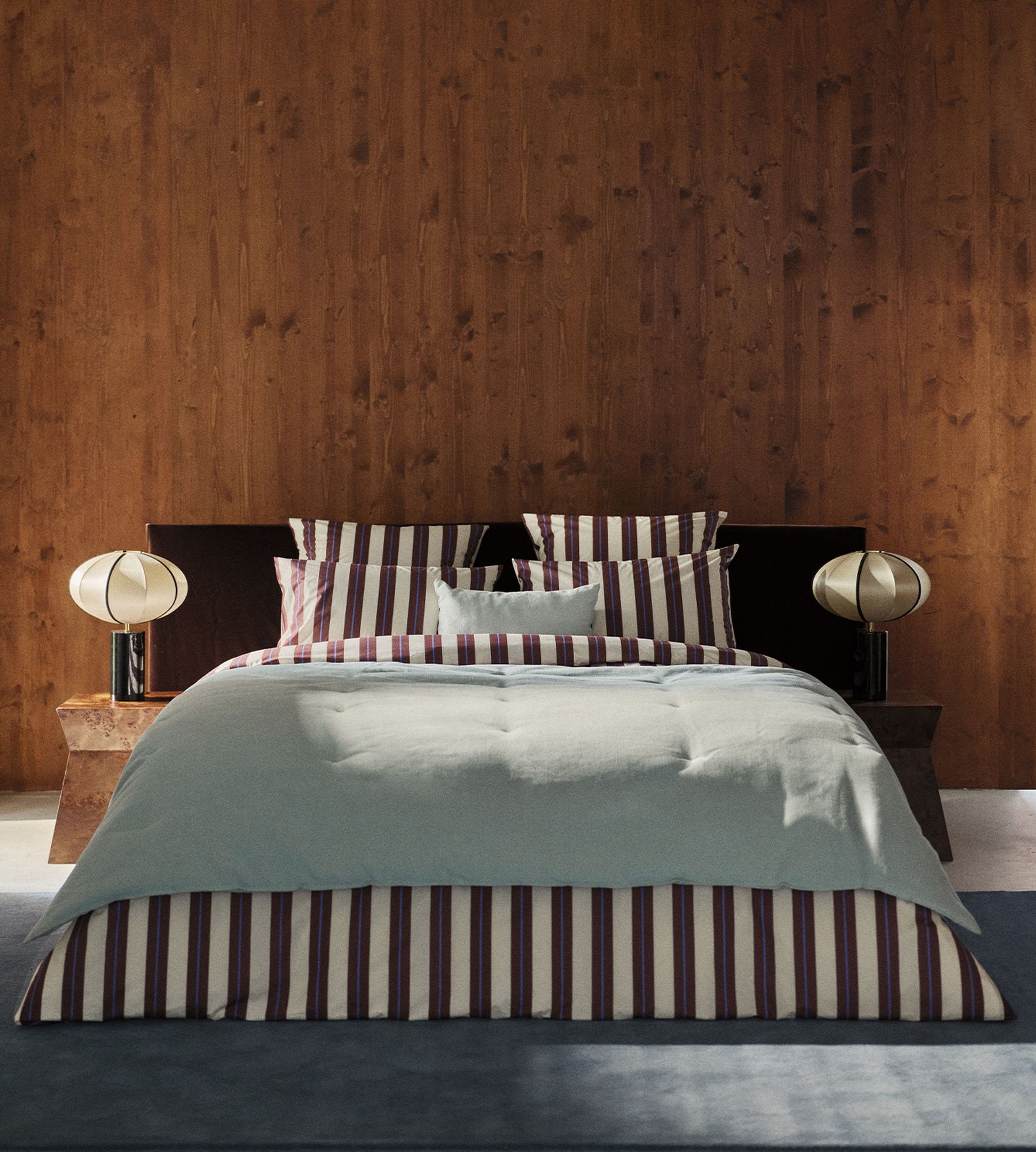 Une chambre moderne avec un mur en bois, une parure de lit rayée rouge et blanche et des lampes rondes posées sur des tables de chevet rustiques.