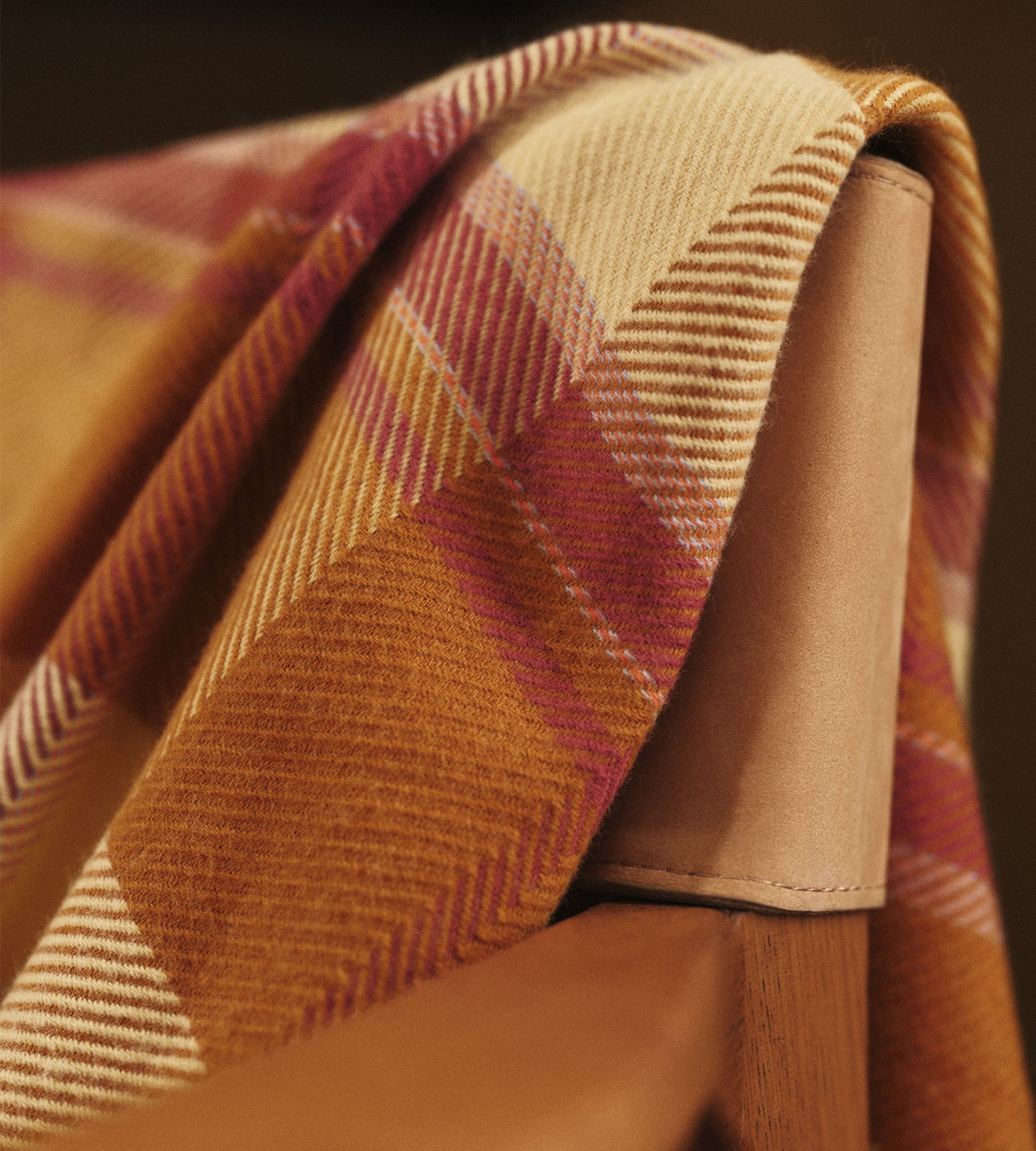 Un tissu à carreaux dans les tons orange et rose est drapé sur le dossier d'une chaise en bois.
