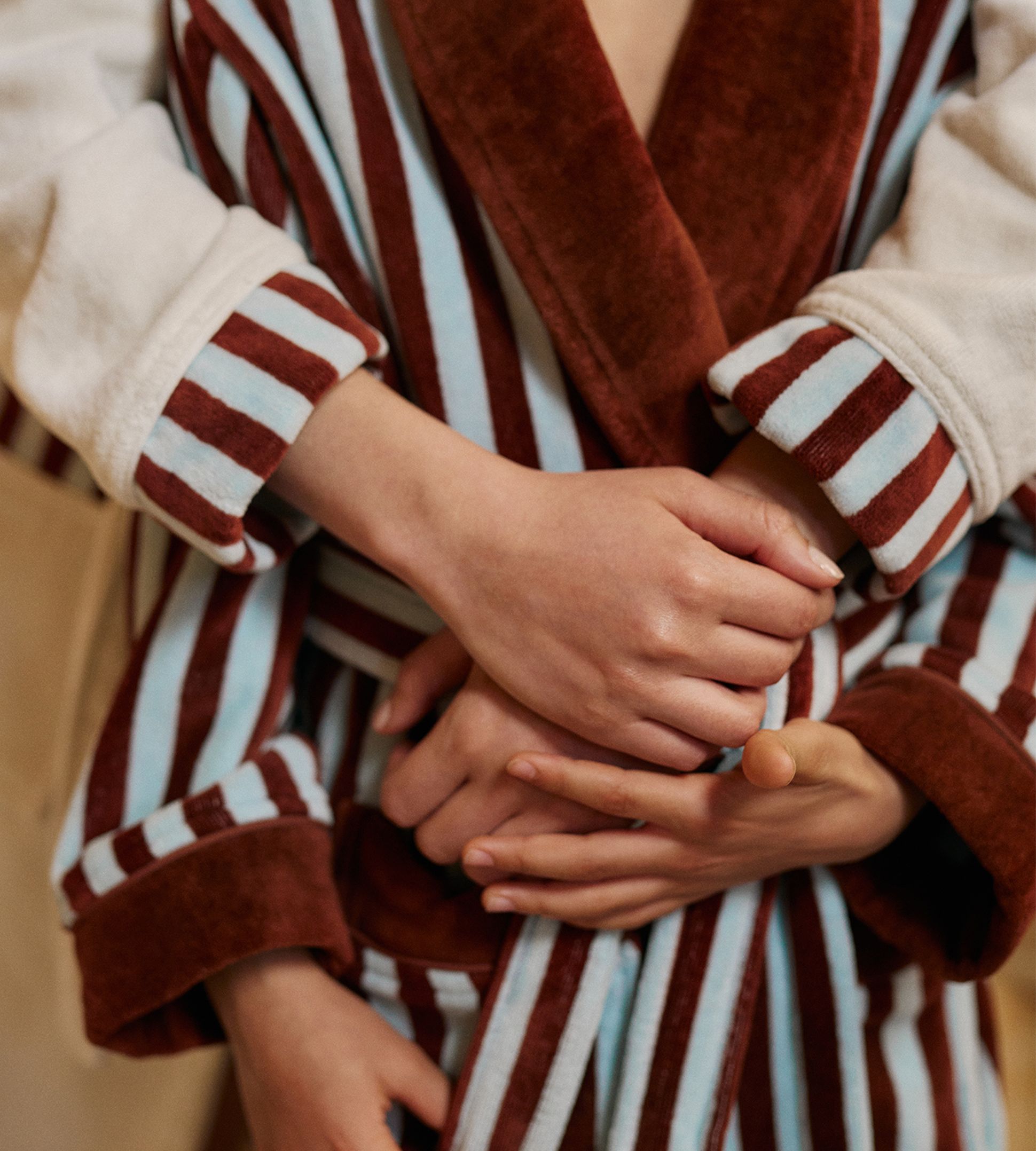 Deux personnes vêtues de robes rayées, l'une marron et blanche, l'autre marron et bleue, s'étreignant tendrement, dans une atmosphère chaleureuse et affectueuse.