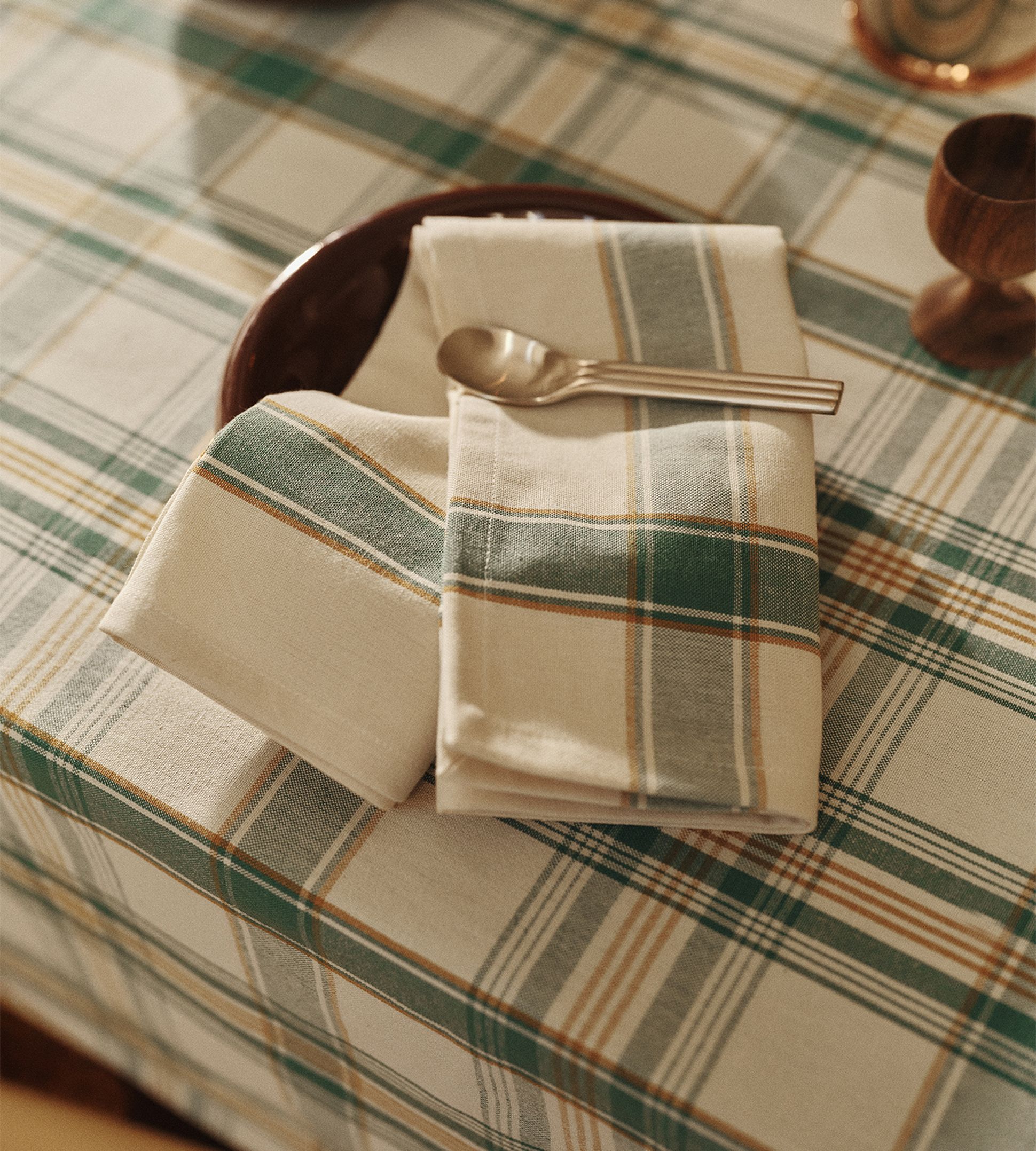 Une nappe à carreaux, accompagnée d'une serviette et d'une cuillère assorties posées sur une assiette marron, créant une table à l'ambiance chaleureuse et rustique.