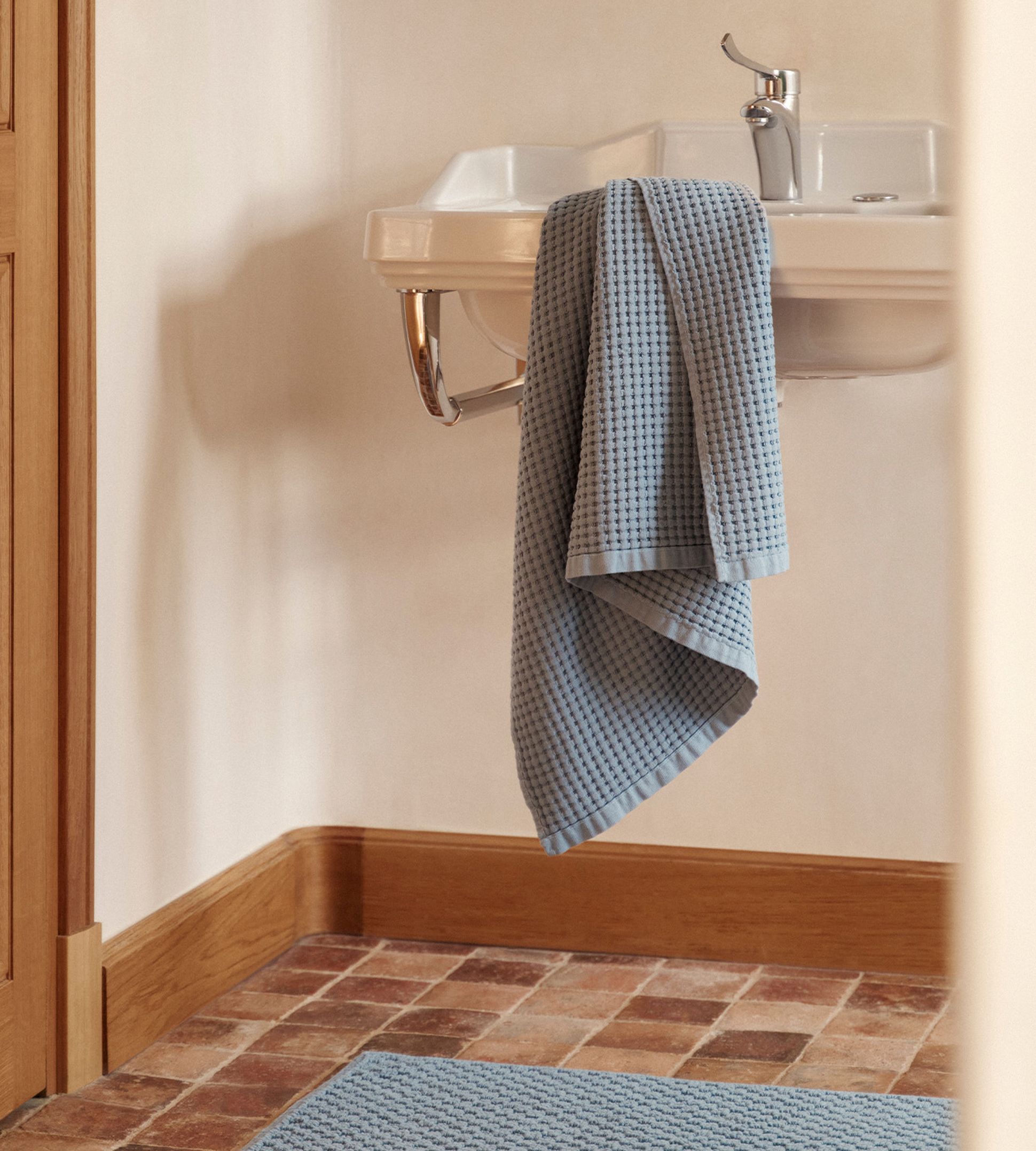 Un lavabo blanc recouvert d'une serviette bleue, posé sur un sol carrelé avec un tapis bleu assorti.