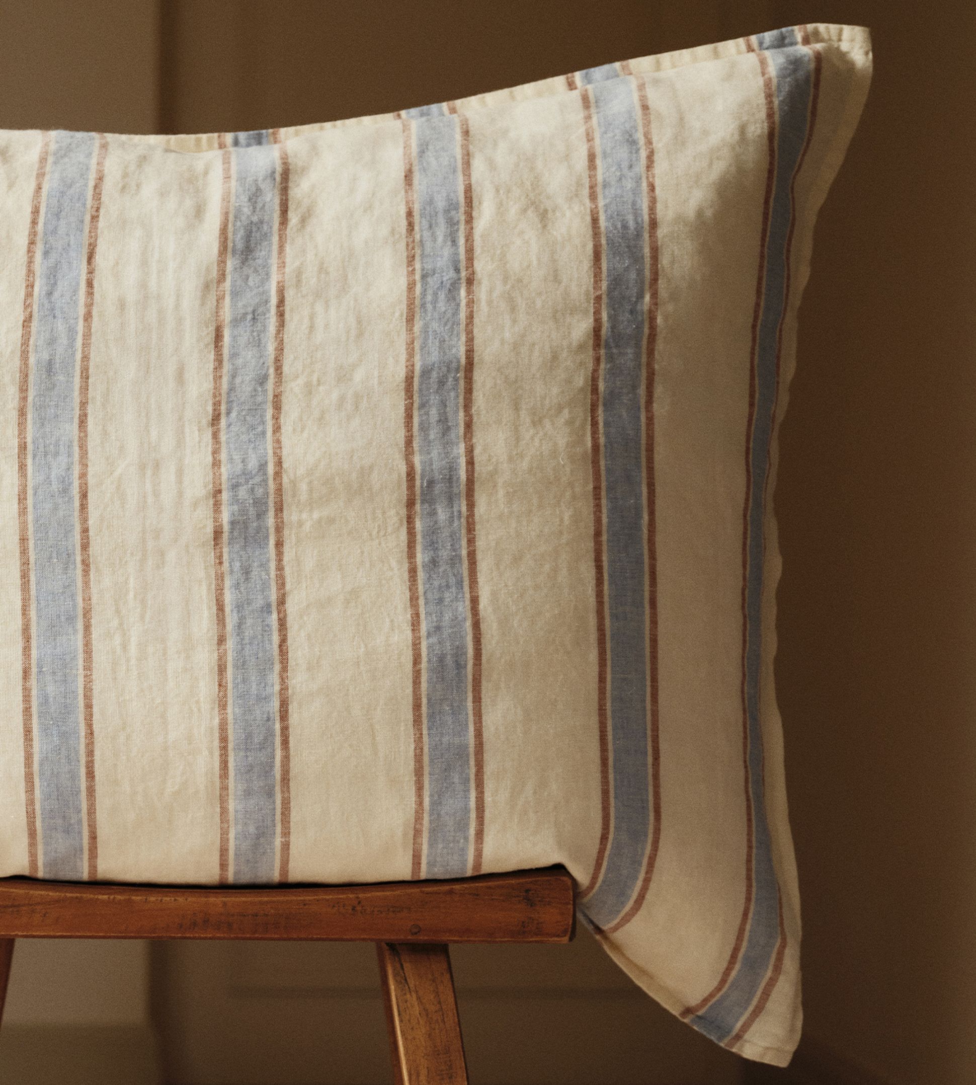 Un coussin à rayures verticales bleues et marron posé sur une chaise en bois.