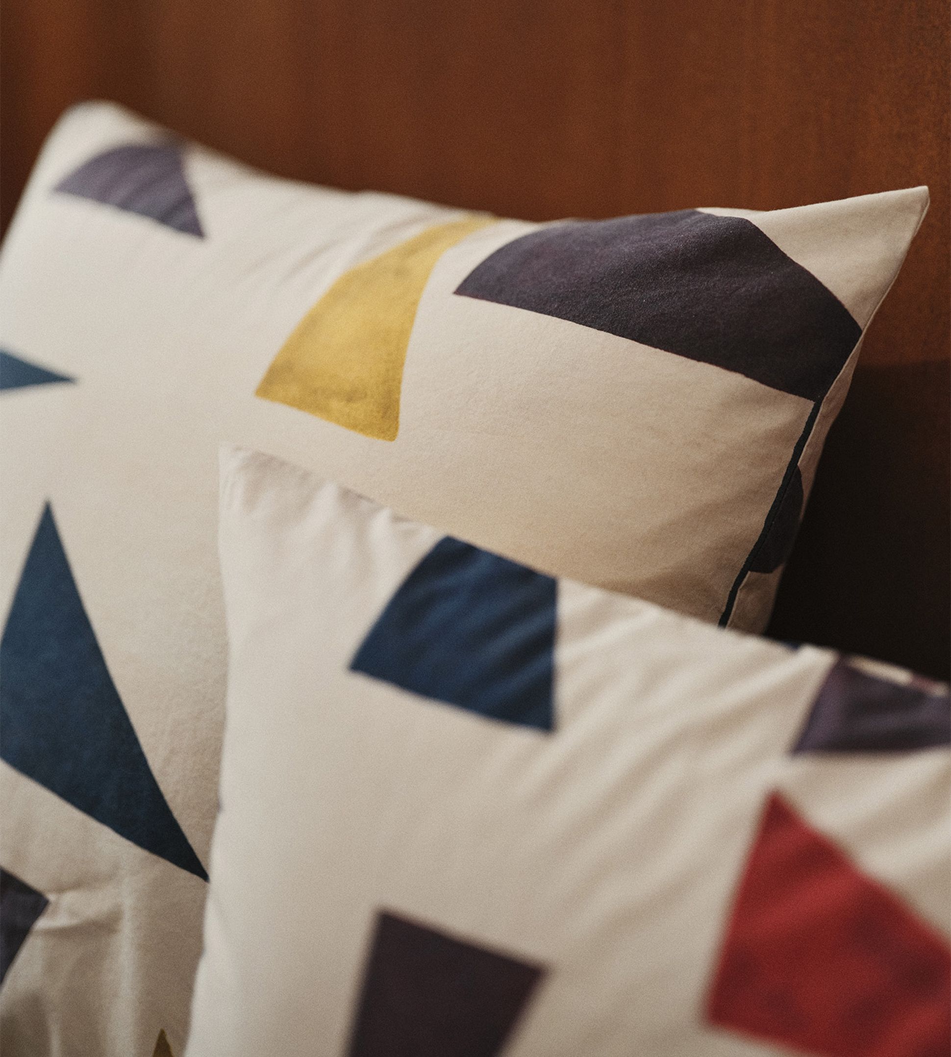 Deux oreillers aux motifs géométriques bleus, jaunes et rouges posés sur un lit à cadre en bois.