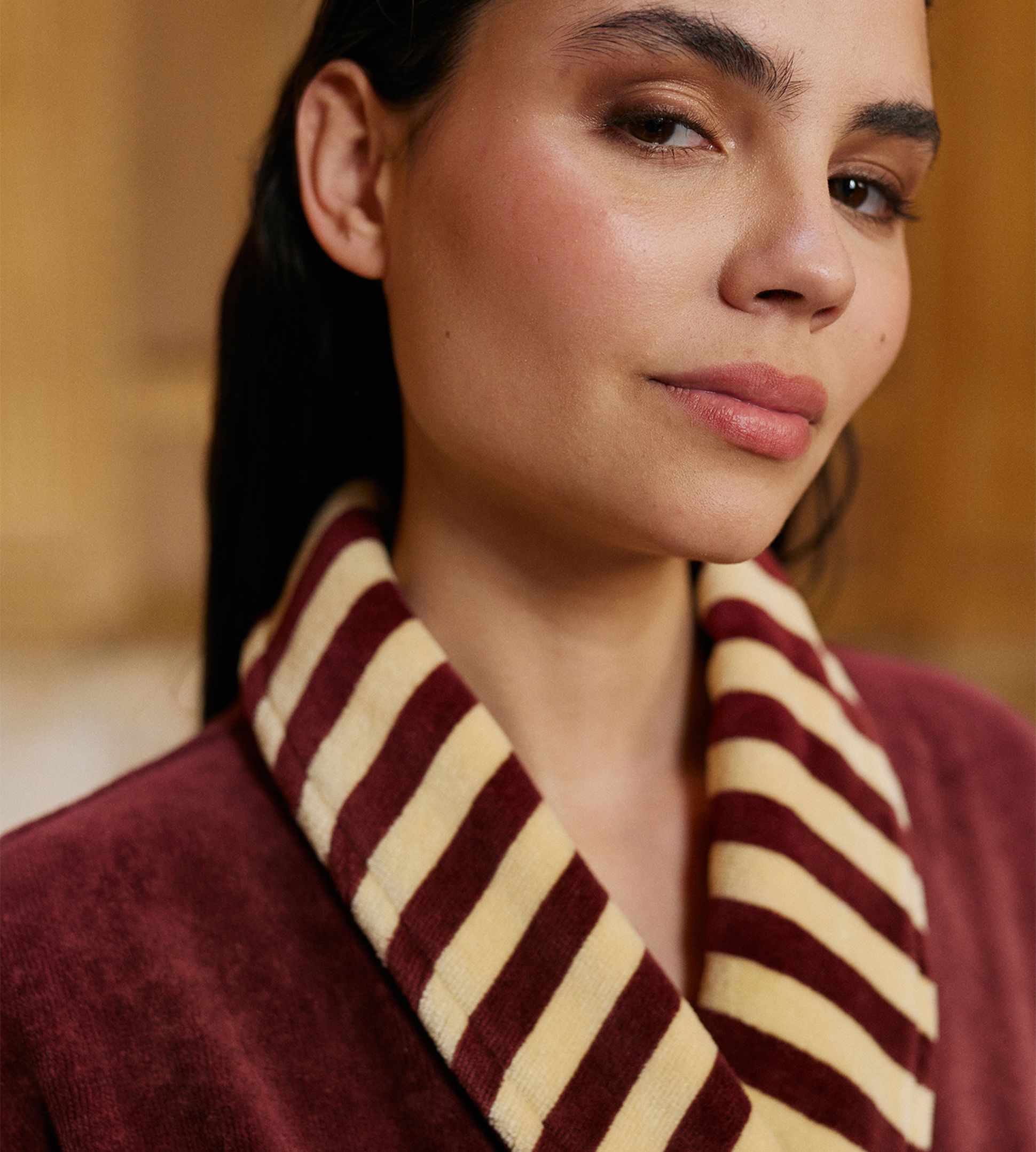 Gros plan sur une personne vêtue d'une robe bordeaux à col rayé bordeaux et beige, avec un cadrage sur le côté droit du visage.