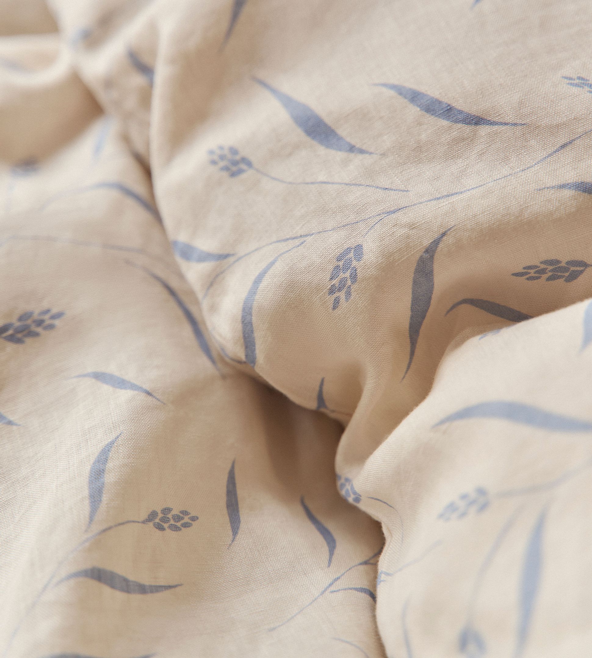 Tissu beige orné d'un motif discret de feuilles et de branches bleues, légèrement froissé.