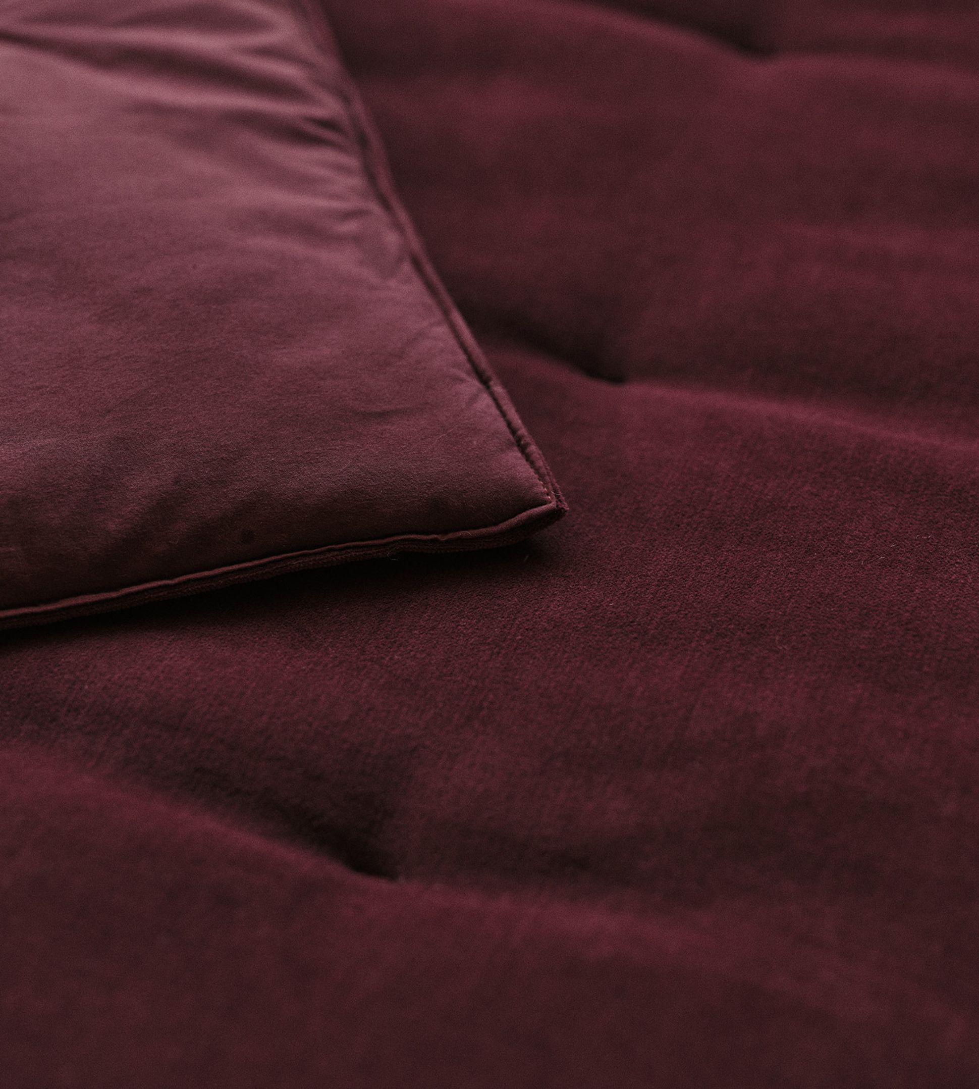 Gros plan sur un tissu de couleur bordeaux, montrant un coin d'un coussin ou d'un oreiller à la texture douce et aux coutures soignées.