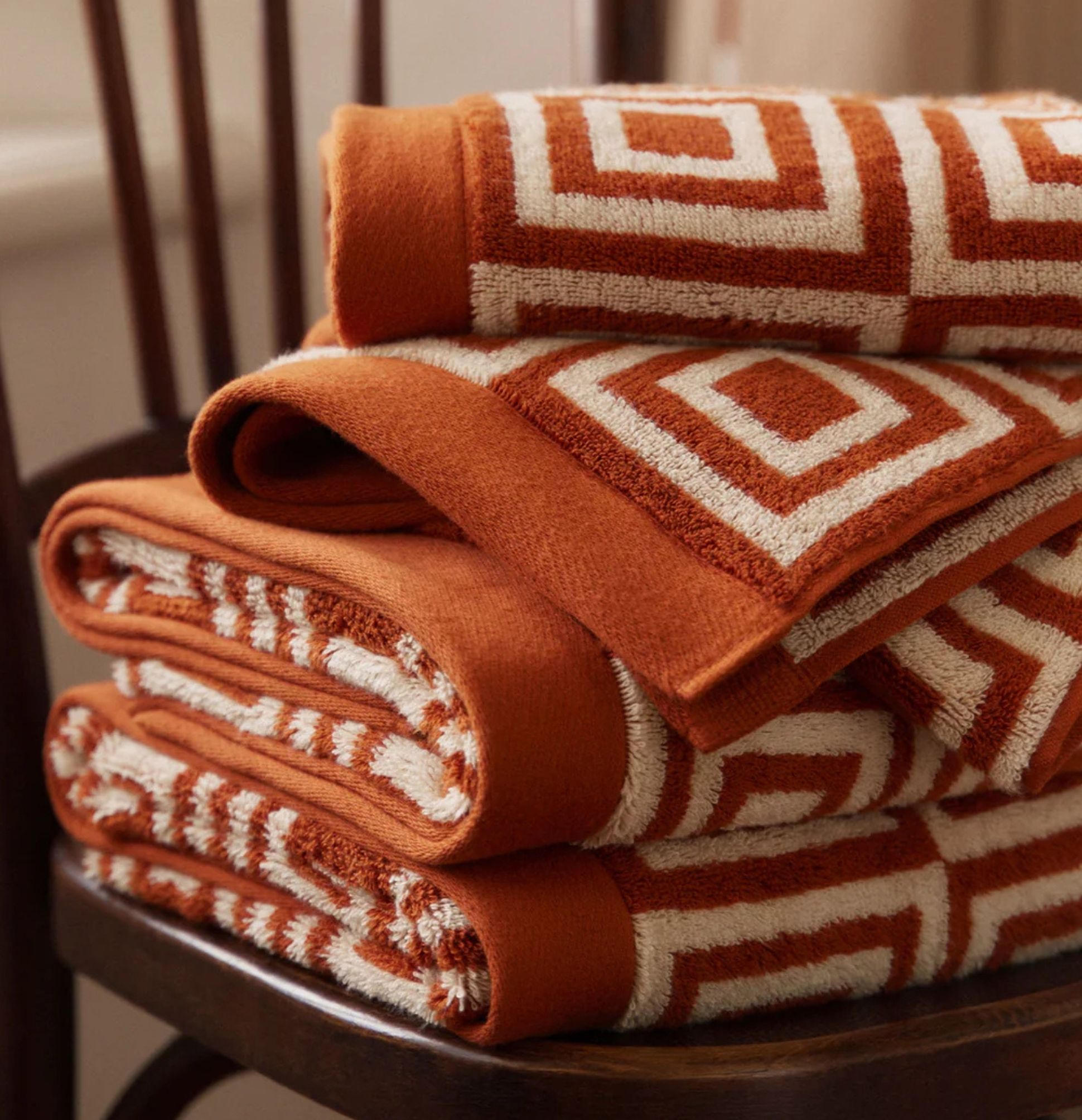 Une pile de serviettes orange et blanches à motifs géométriques, soigneusement pliées sur une chaise en bois.