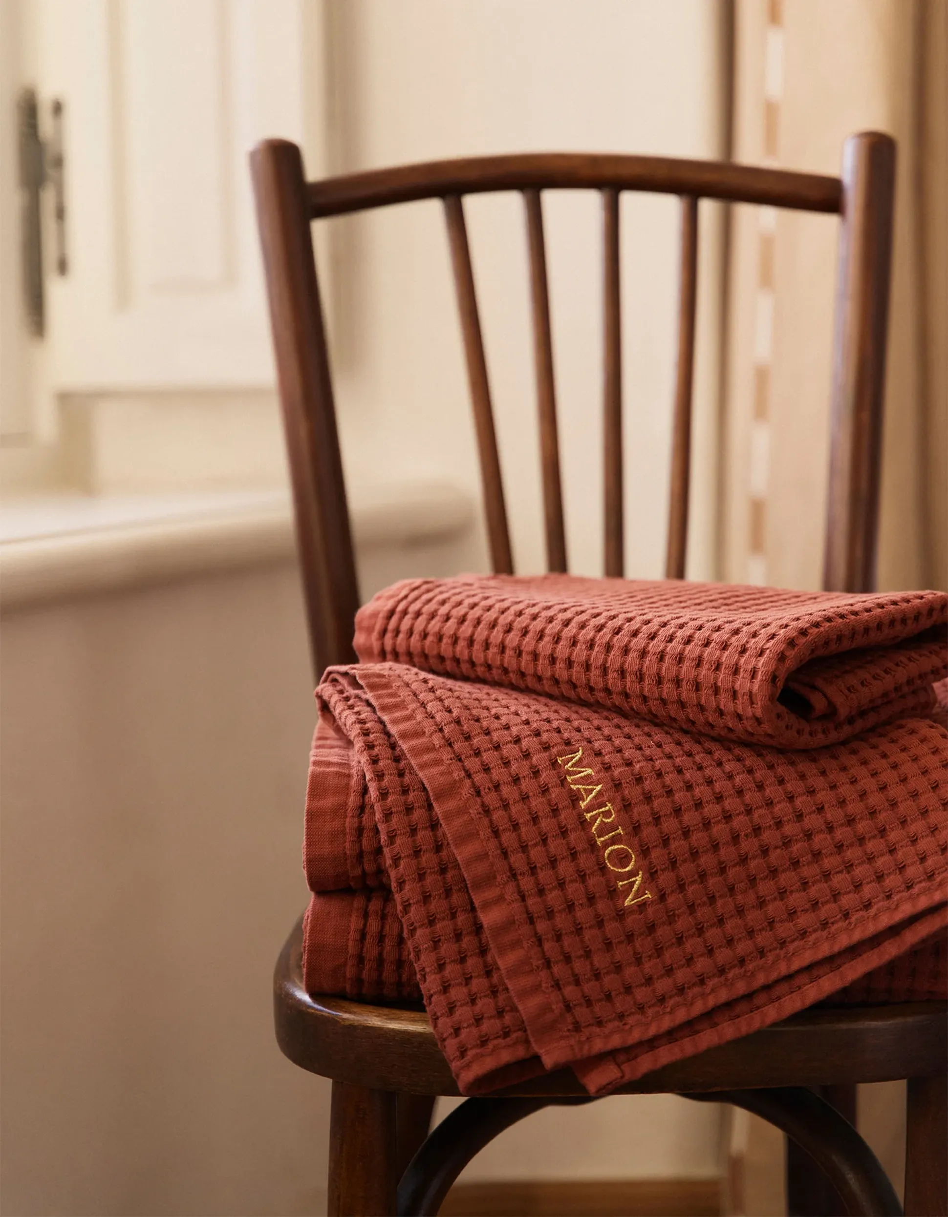 Set de serviette nid d'abeille Terracotta avec une des serviettes brodée avec le nom "Marion" sur une chaise en bois