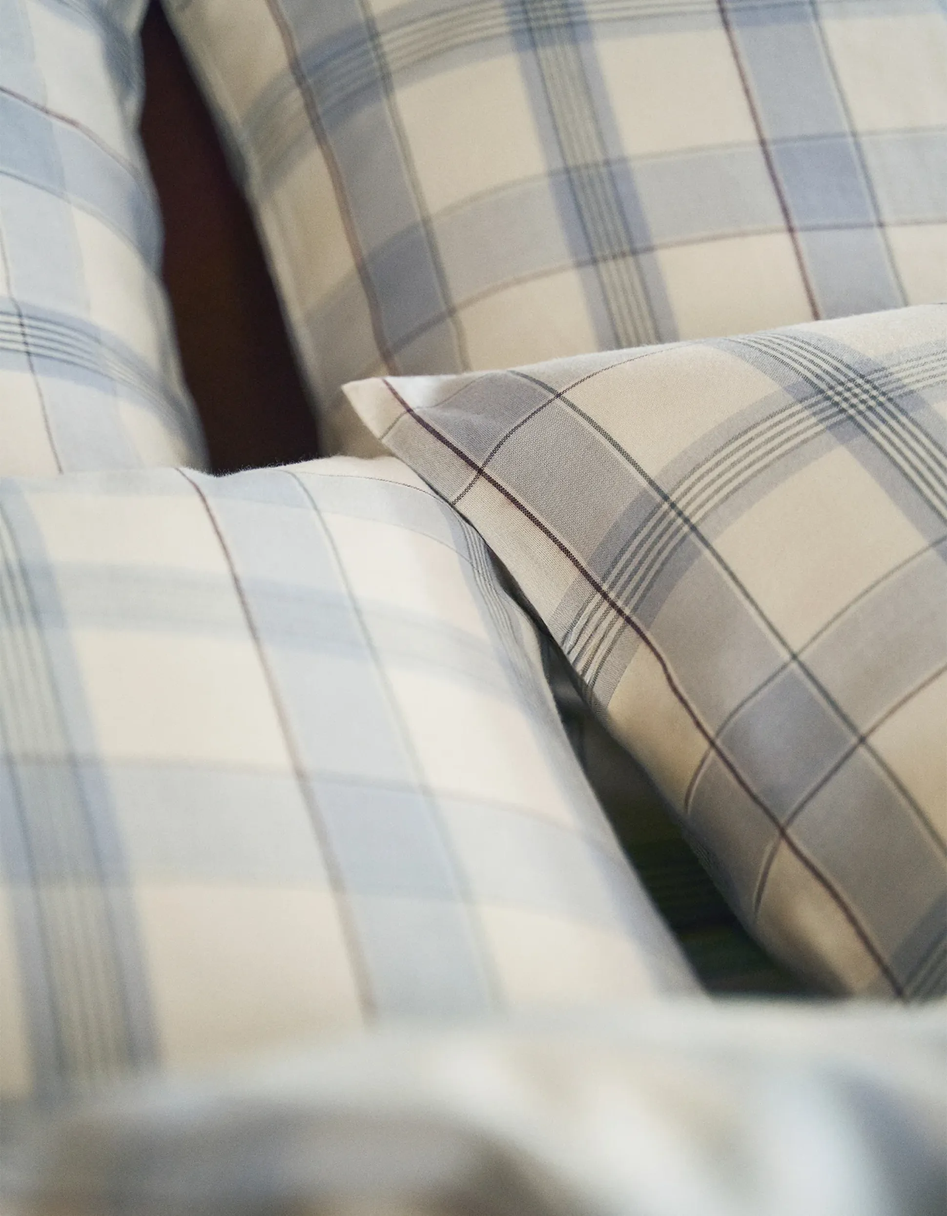 Trois oreillers à carreaux bleus et beiges, disposés les uns à côté des autres sur un lit.