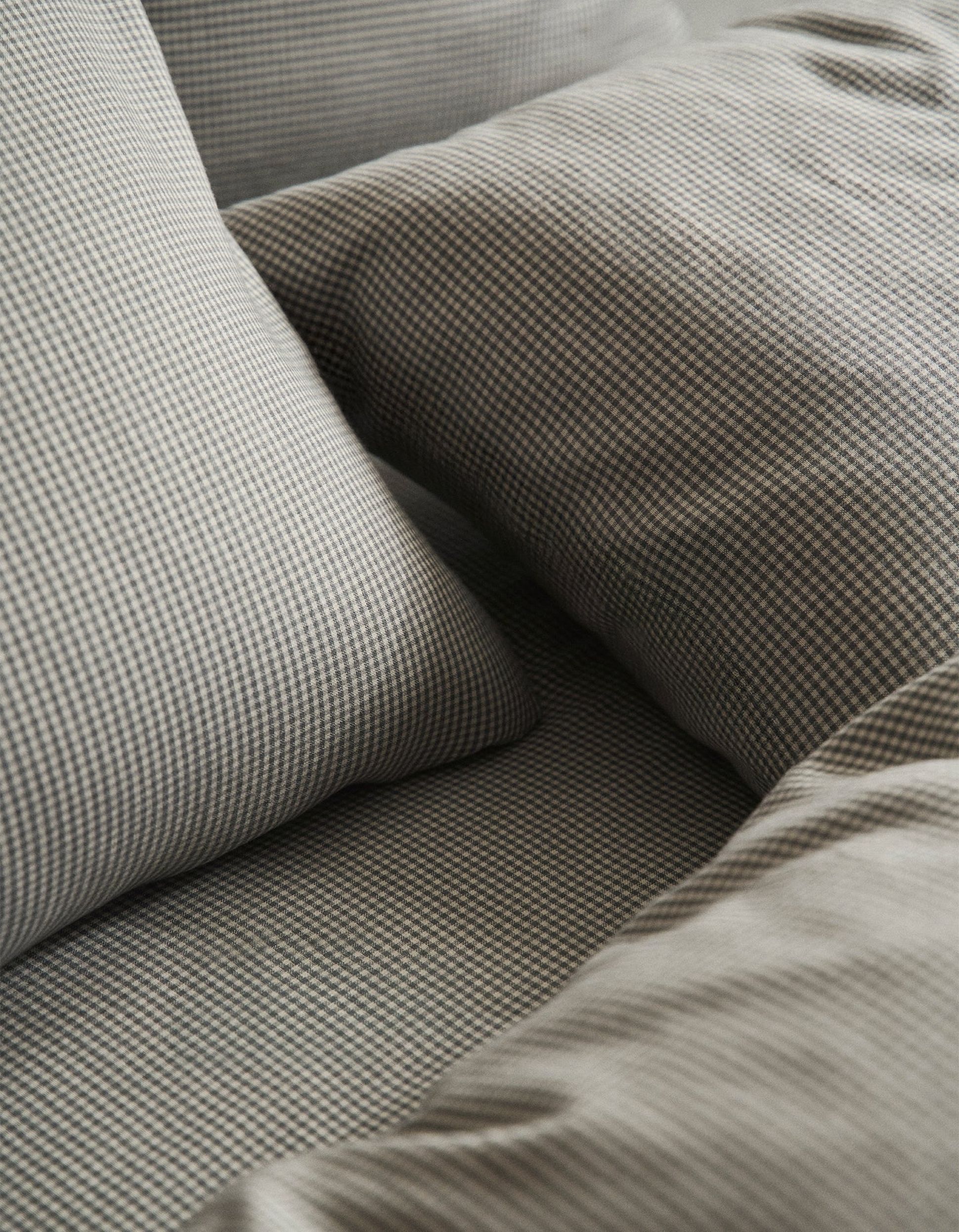 Gros plan sur un lit recouvert de draps et d'oreillers à carreaux gris, qui se distinguent par leur motif texturé et leur aspect chaleureux.