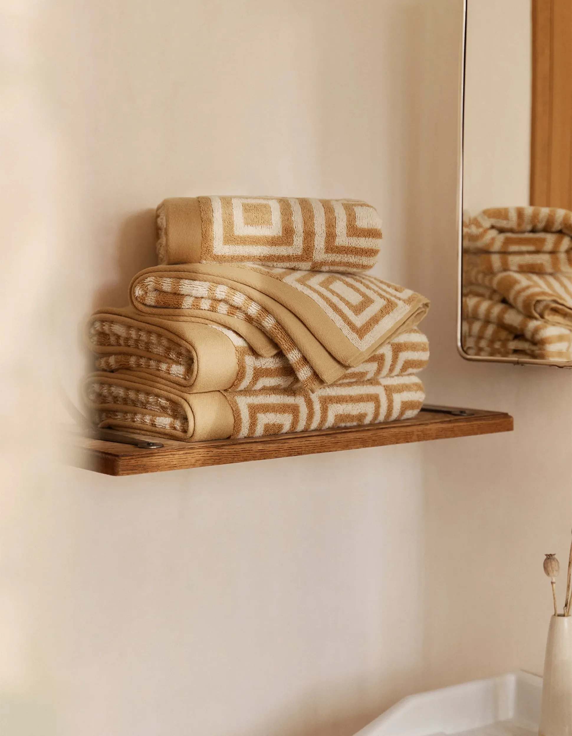 Serviettes à motifs géométriques pliées en beige et blanc sur une étagère en bois, reflétées dans un miroir à proximité.