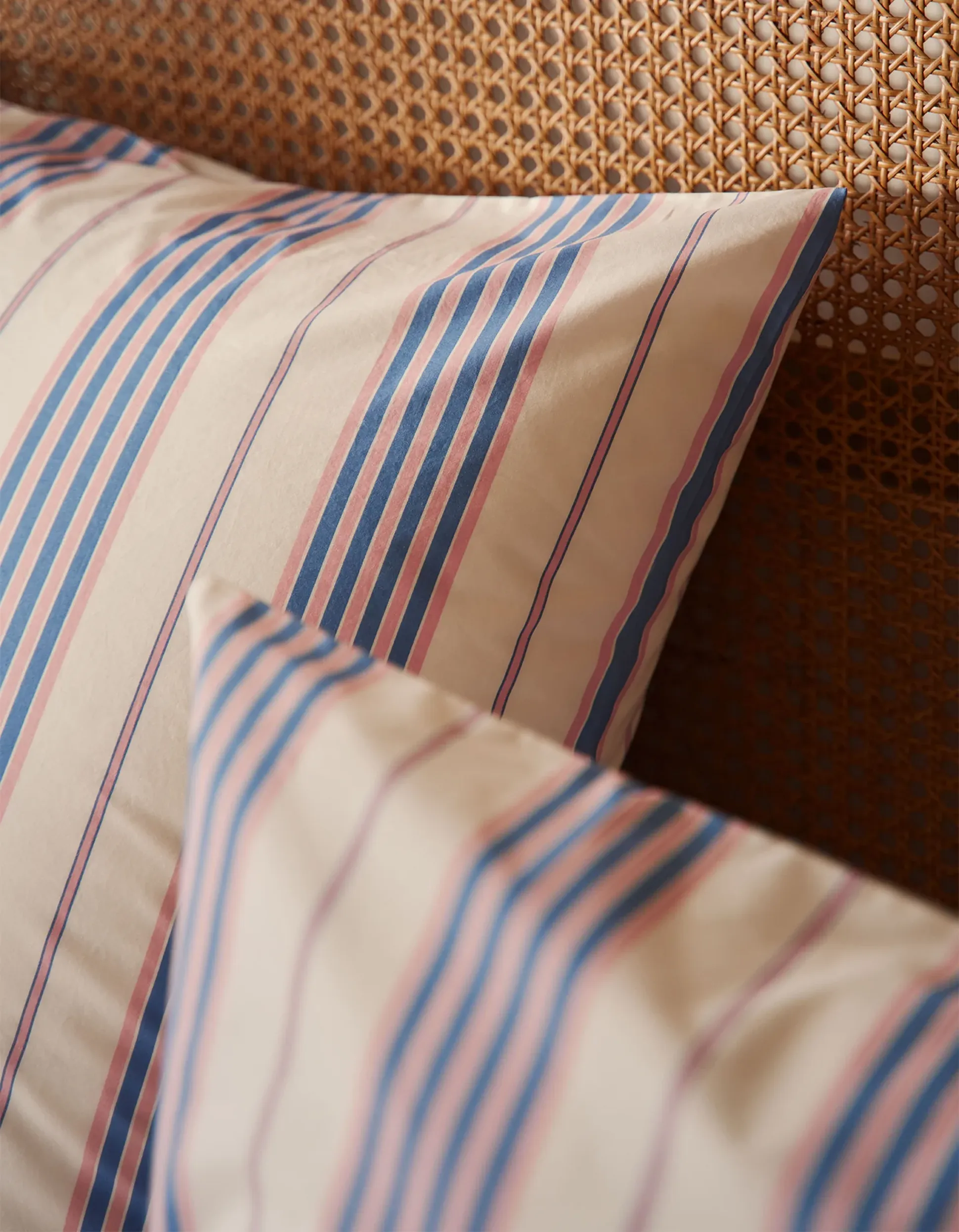 Des coussins rayés dans des tons bleus et roses reposent sur une tête de lit en osier, créant une ambiance chaleureuse et accueillante dans la chambre.