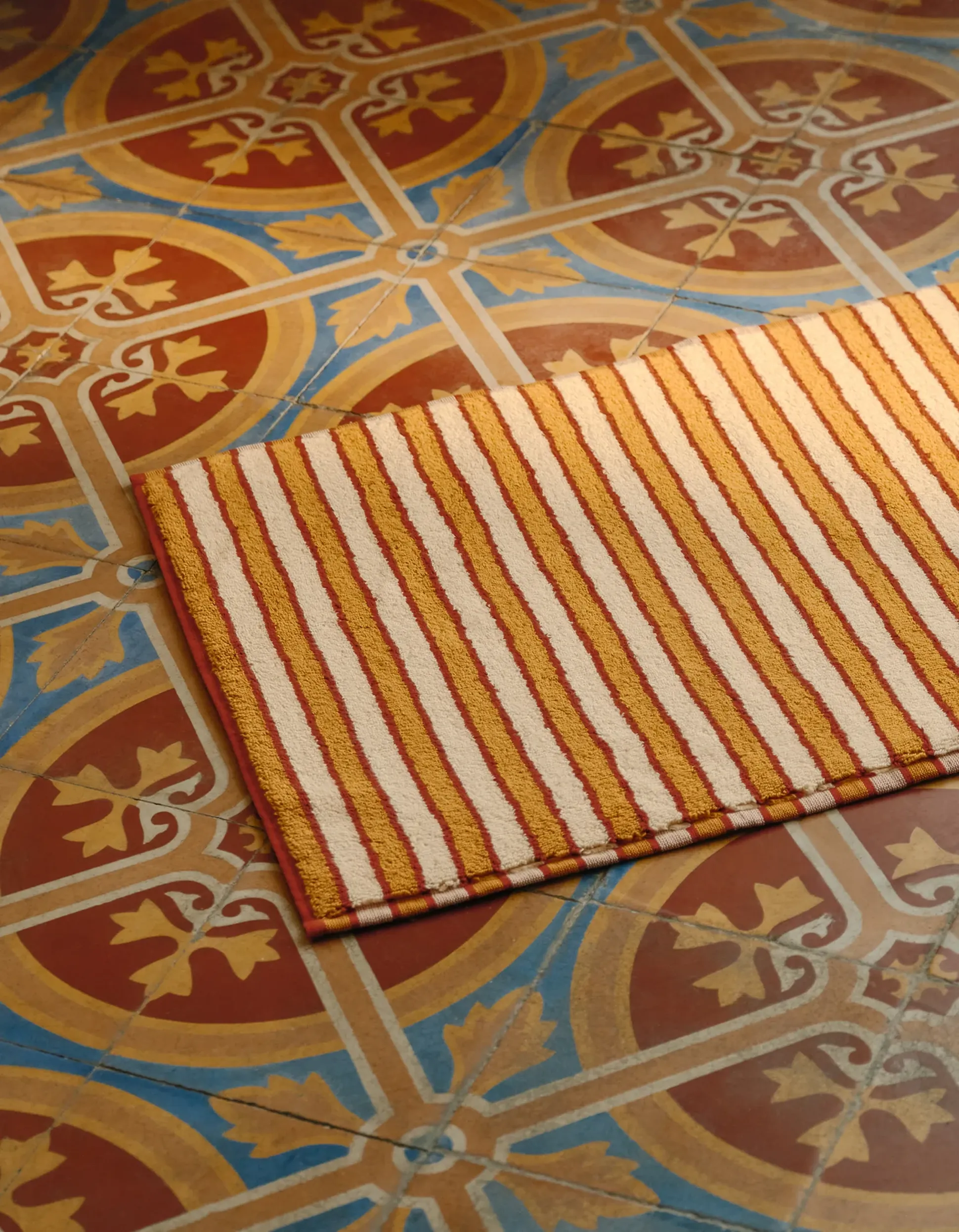 Tapis rayé avec des lignes rouges et beiges sur des carreaux géométriques colorés, ornés de motifs circulaires bleus et orange et de motifs floraux.