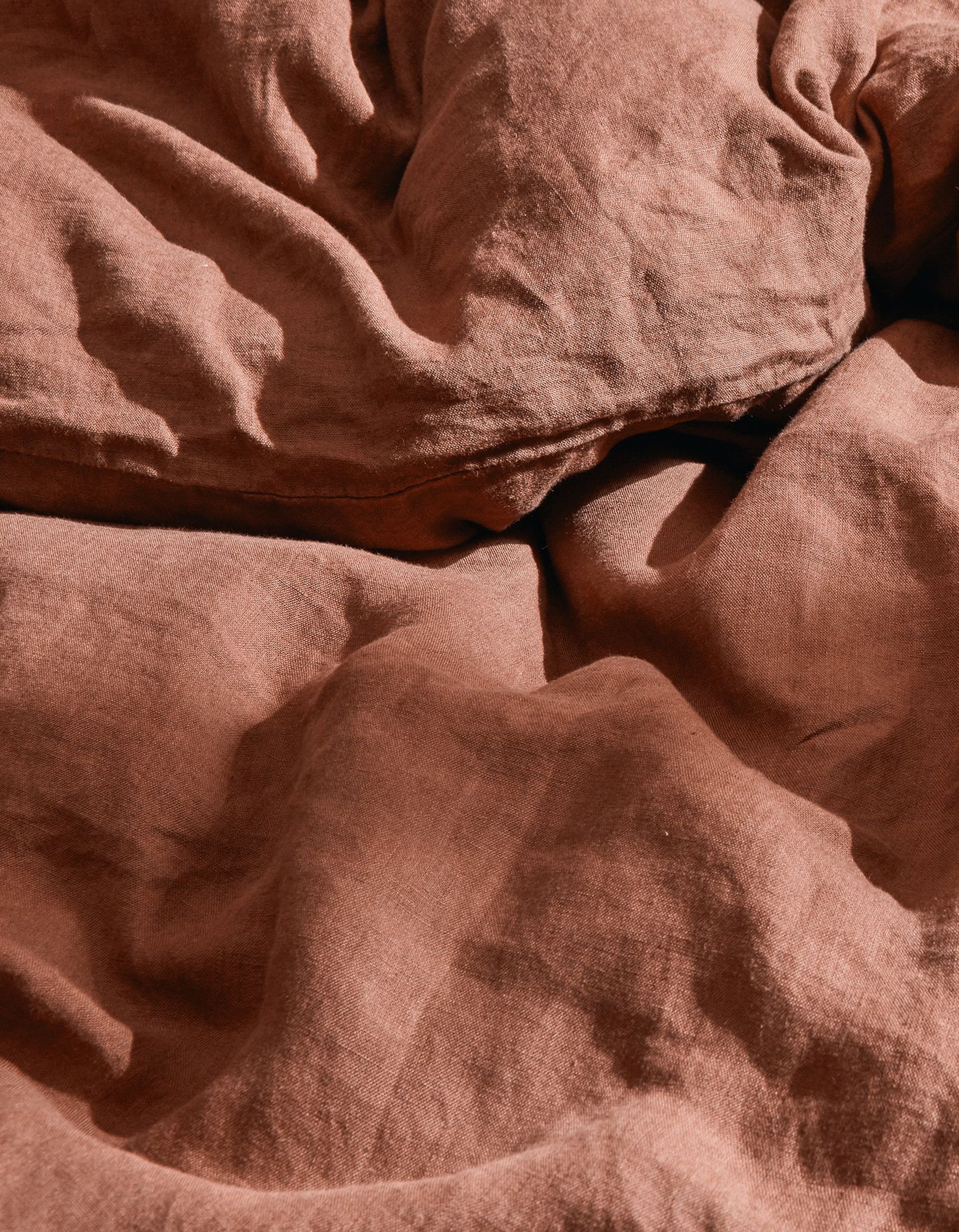 Gros plan sur un tissu en lin froissé, de couleur rouille, dont la texture est bien visible et qui présente de légères ombres.