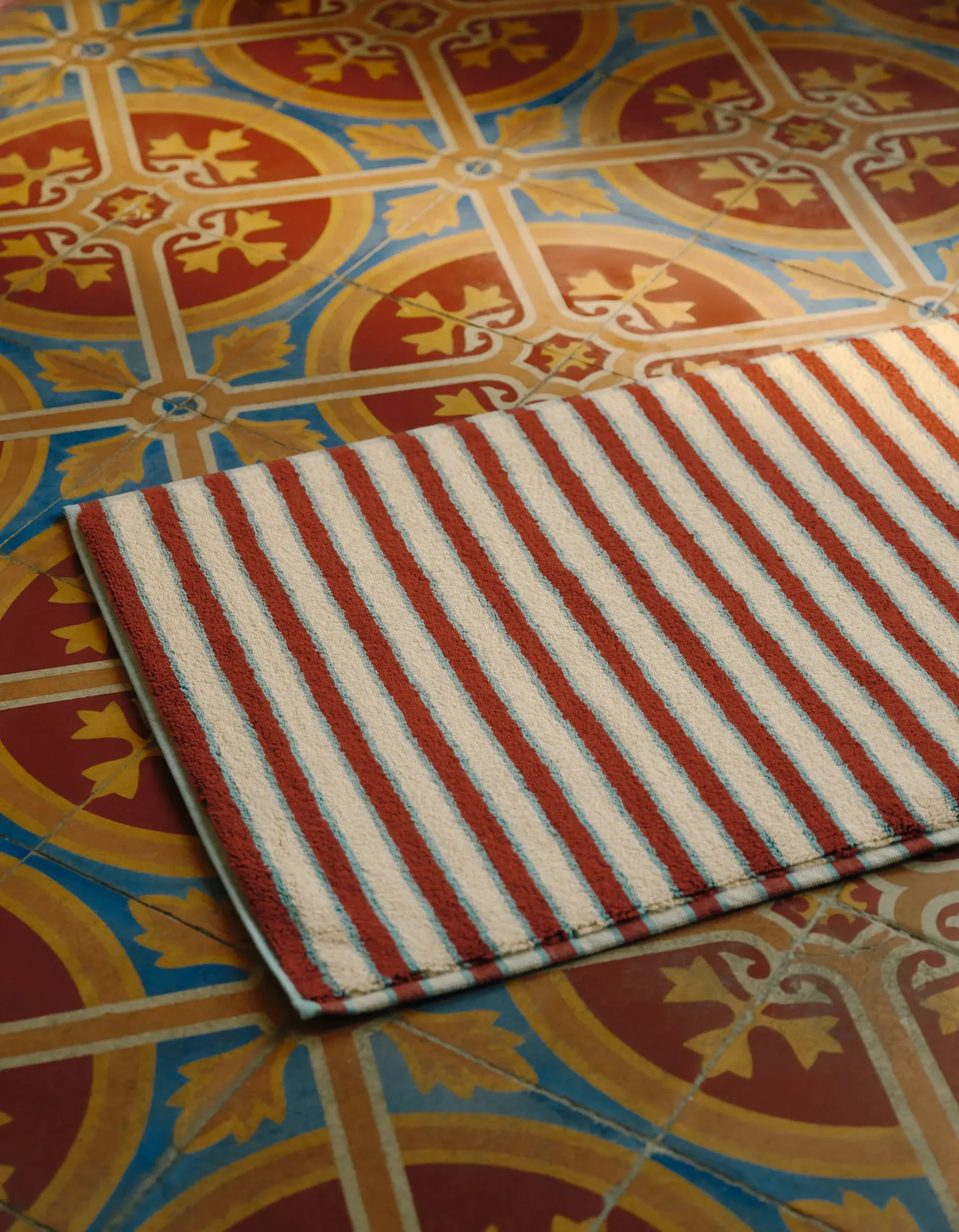 Tapis rayé posé sur un sol en mosaïque colorée aux motifs complexes, composés de figures géométriques et florales rouges, bleues et dorées.