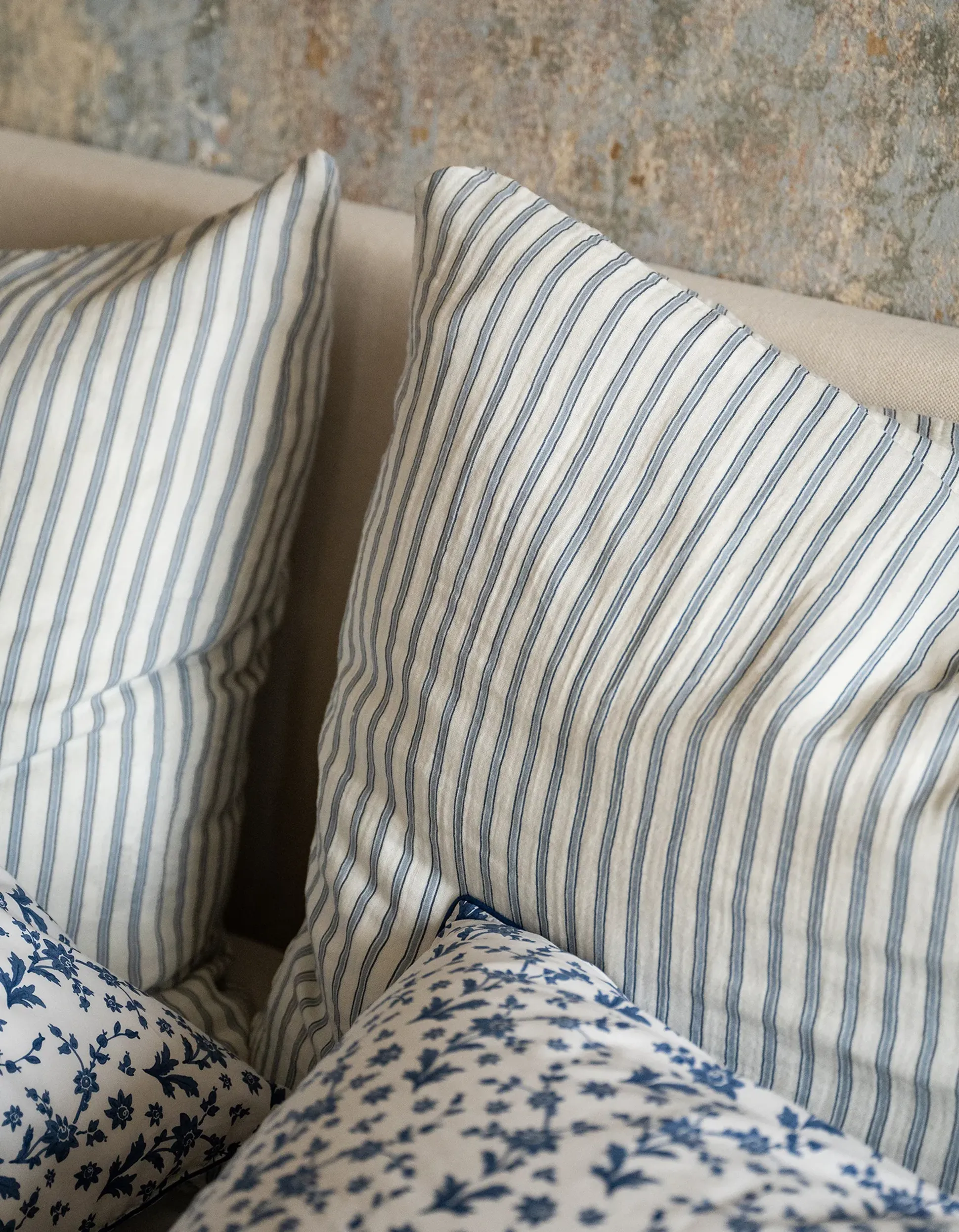 Des coussins rayés bleus et blancs adossés à un mur texturé, associés à un coussin à motifs floraux.