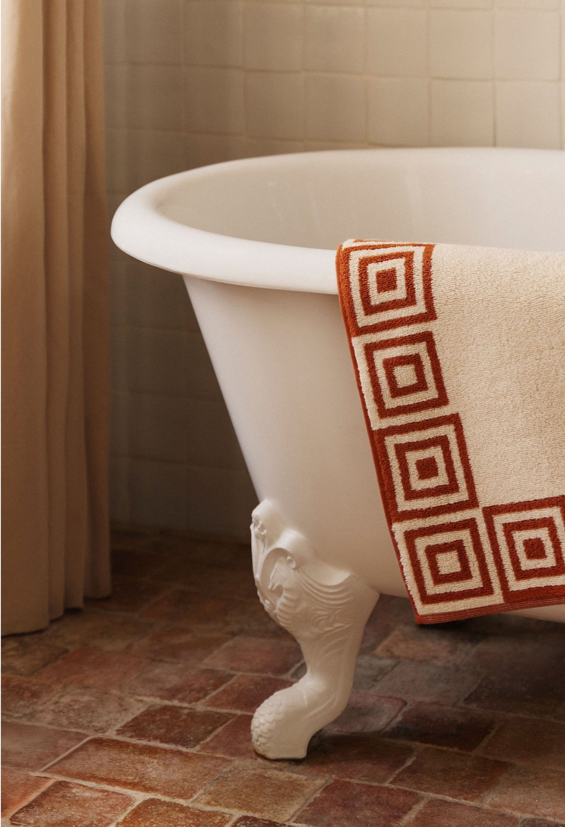 Une baignoire blanche sur pieds, avec une serviette décorative drapée sur le rebord, posée sur un sol carrelé.