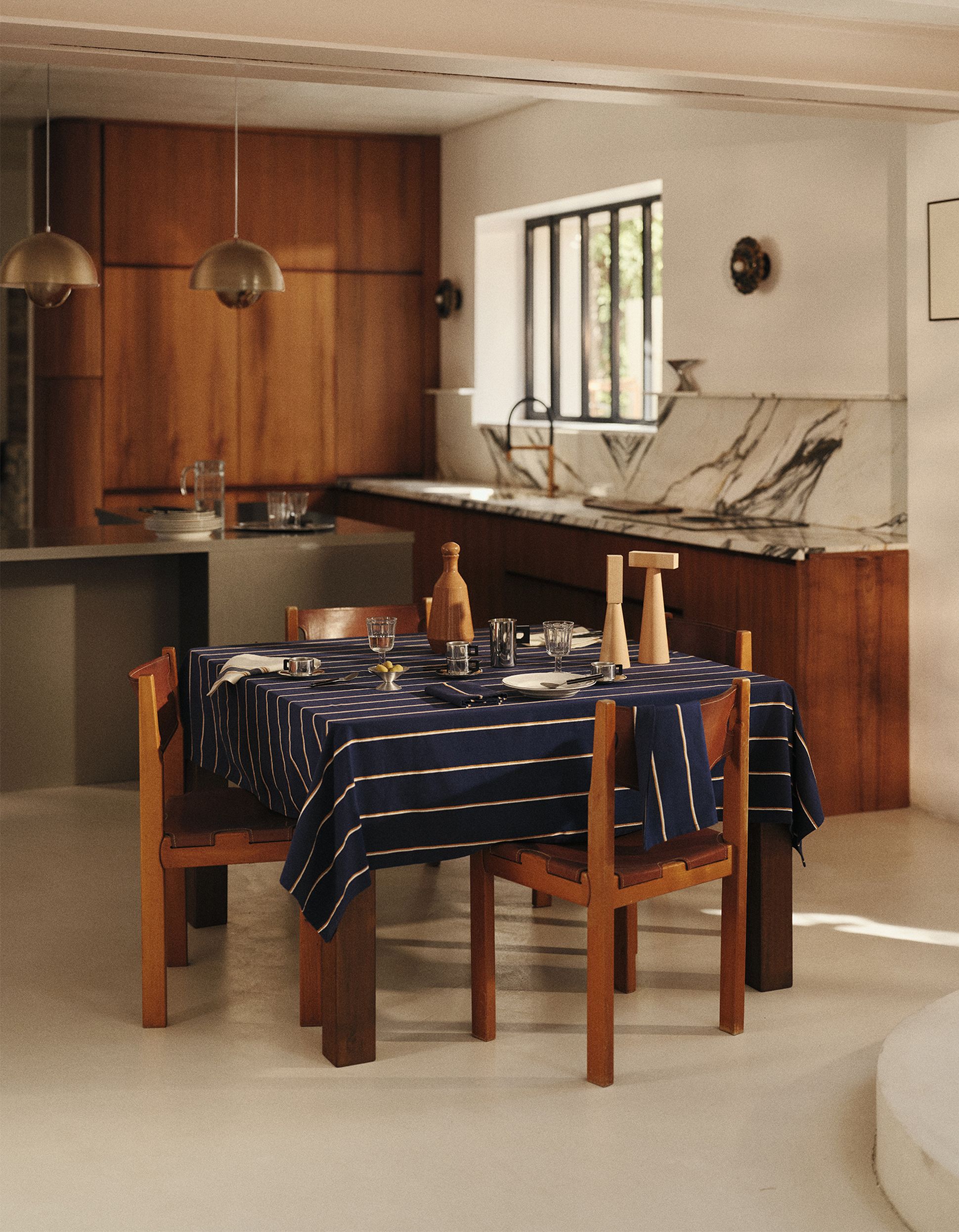 Une cuisine moderne avec un plan de travail en marbre, des placards en bois et une table à manger recouverte d'une nappe à rayures bleues, dressée pour un repas.