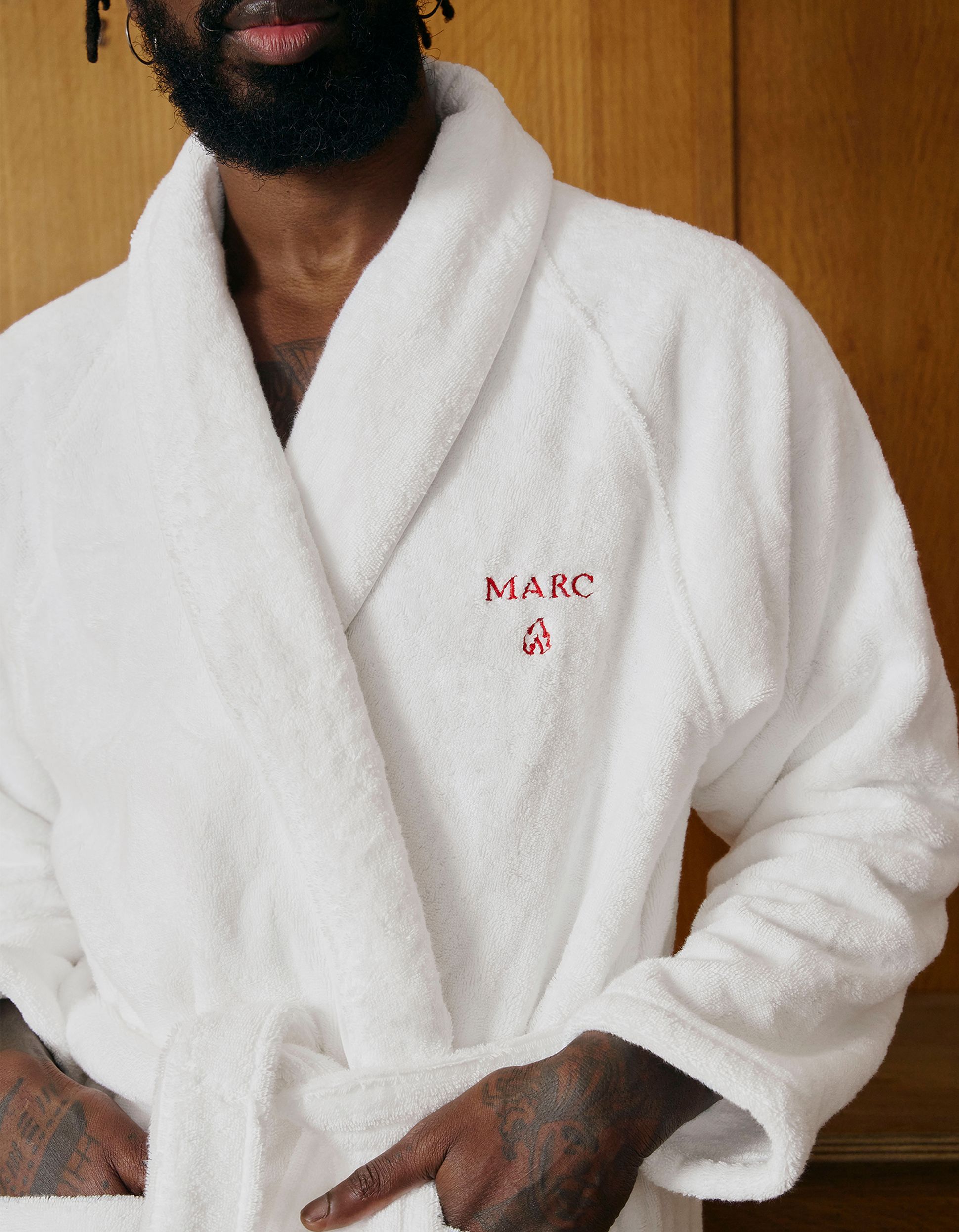 Person wearing a white bathrobe with "MARC" embroidered in red on the chest, standing against a wooden background.