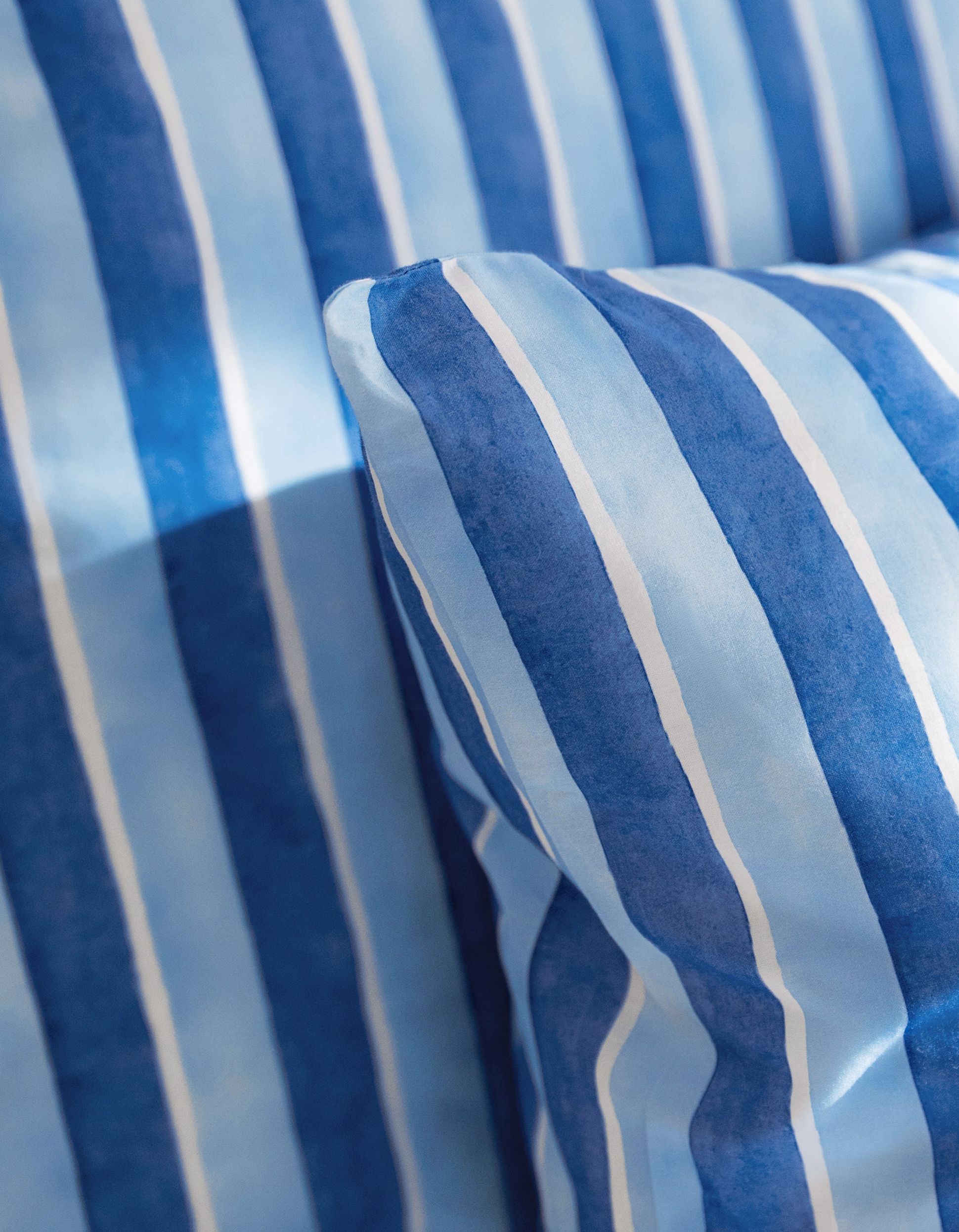 Gros plan sur un oreiller et un drap à rayures verticales bleues et blanches, formant un motif marin.