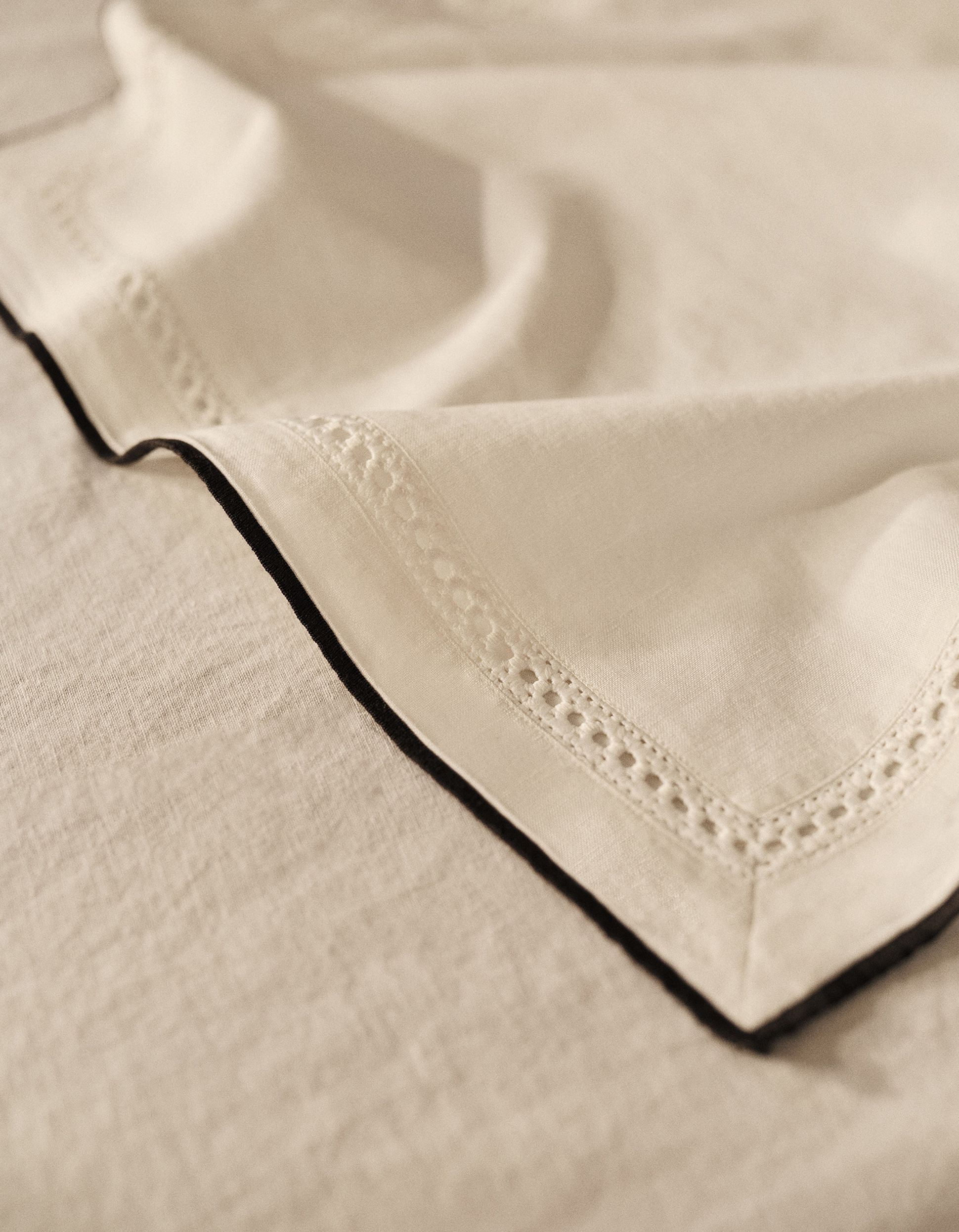 Gros plan sur un tissu beige clair orné de dentelle finement travaillée sur les bords, délicatement plissé sur une surface texturée assortie.