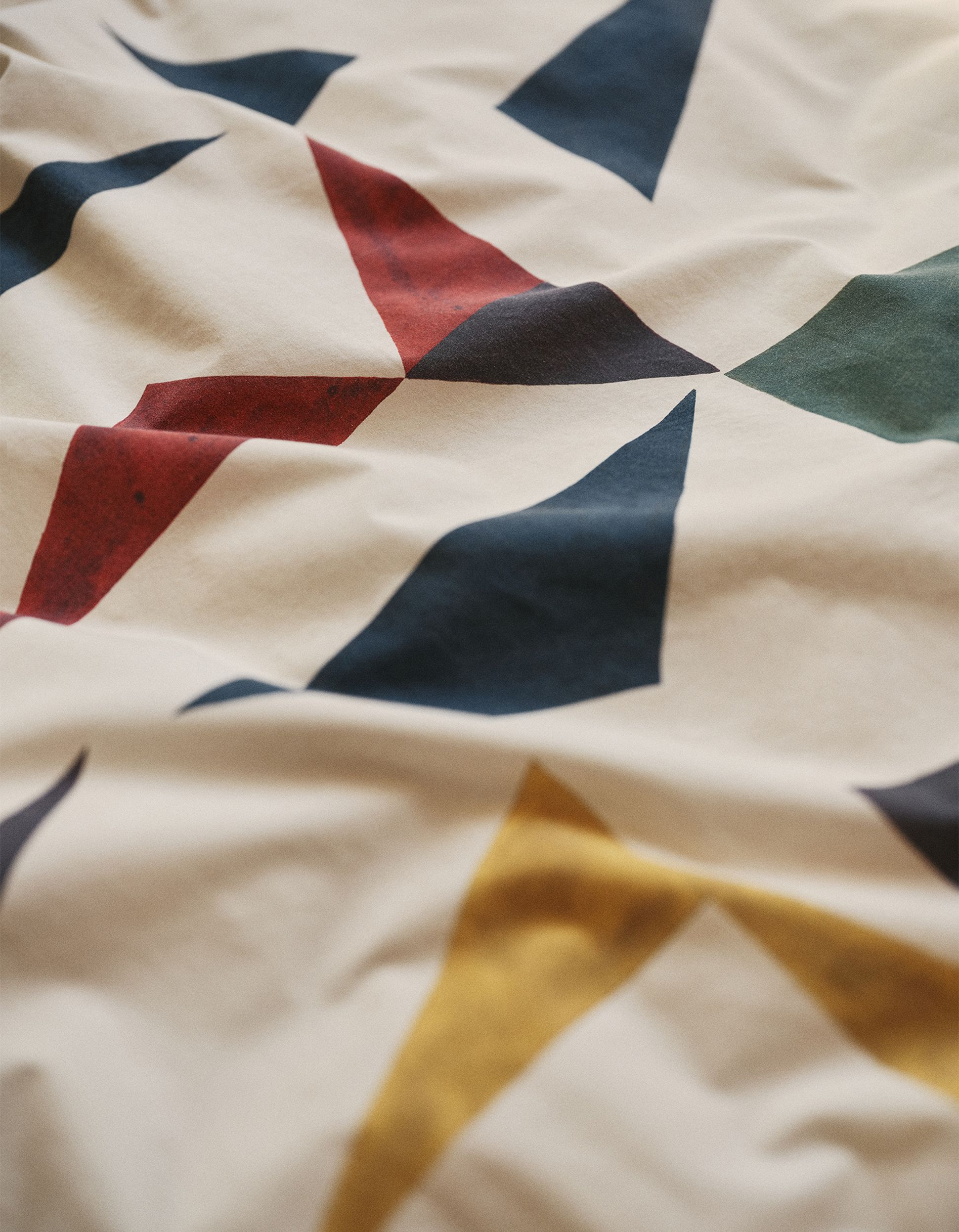 Gros plan sur un tissu présentant des motifs géométriques abstraits dans les tons rouge, bleu, jaune et vert sur un fond crème, avec des plis délicats.