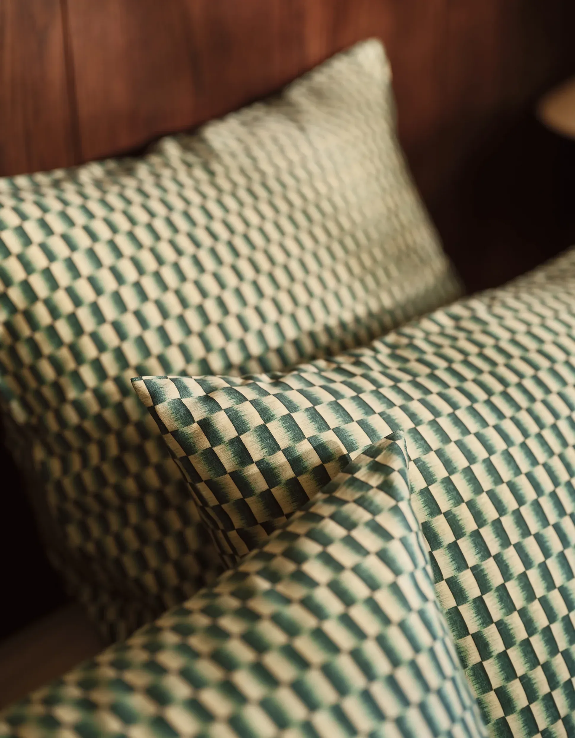 Deux oreillers à motif damier vert et beige, posés sur un lit en bois.
