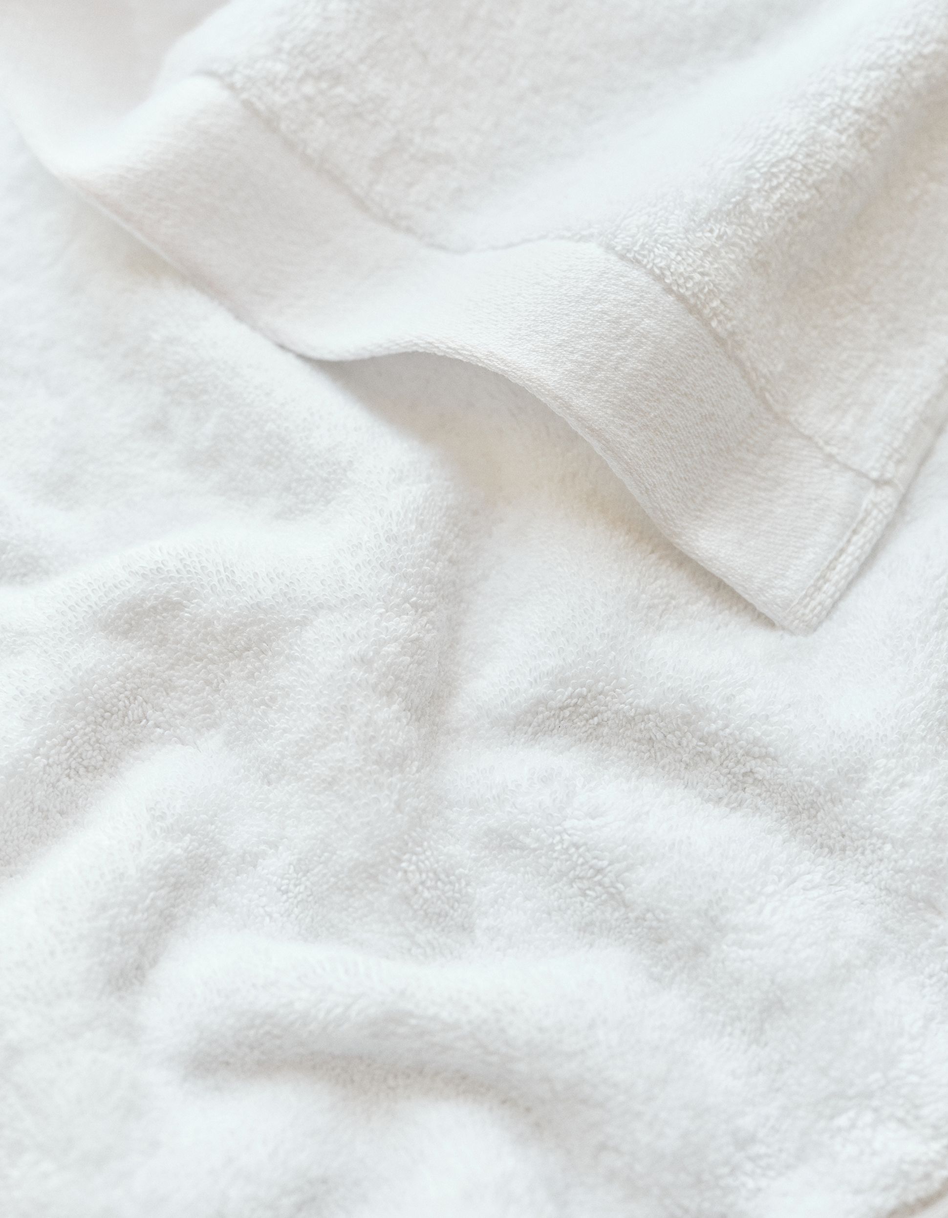 Soft, white towel with a textured surface and folded corner, creating subtle shadows and a sense of plush coziness.