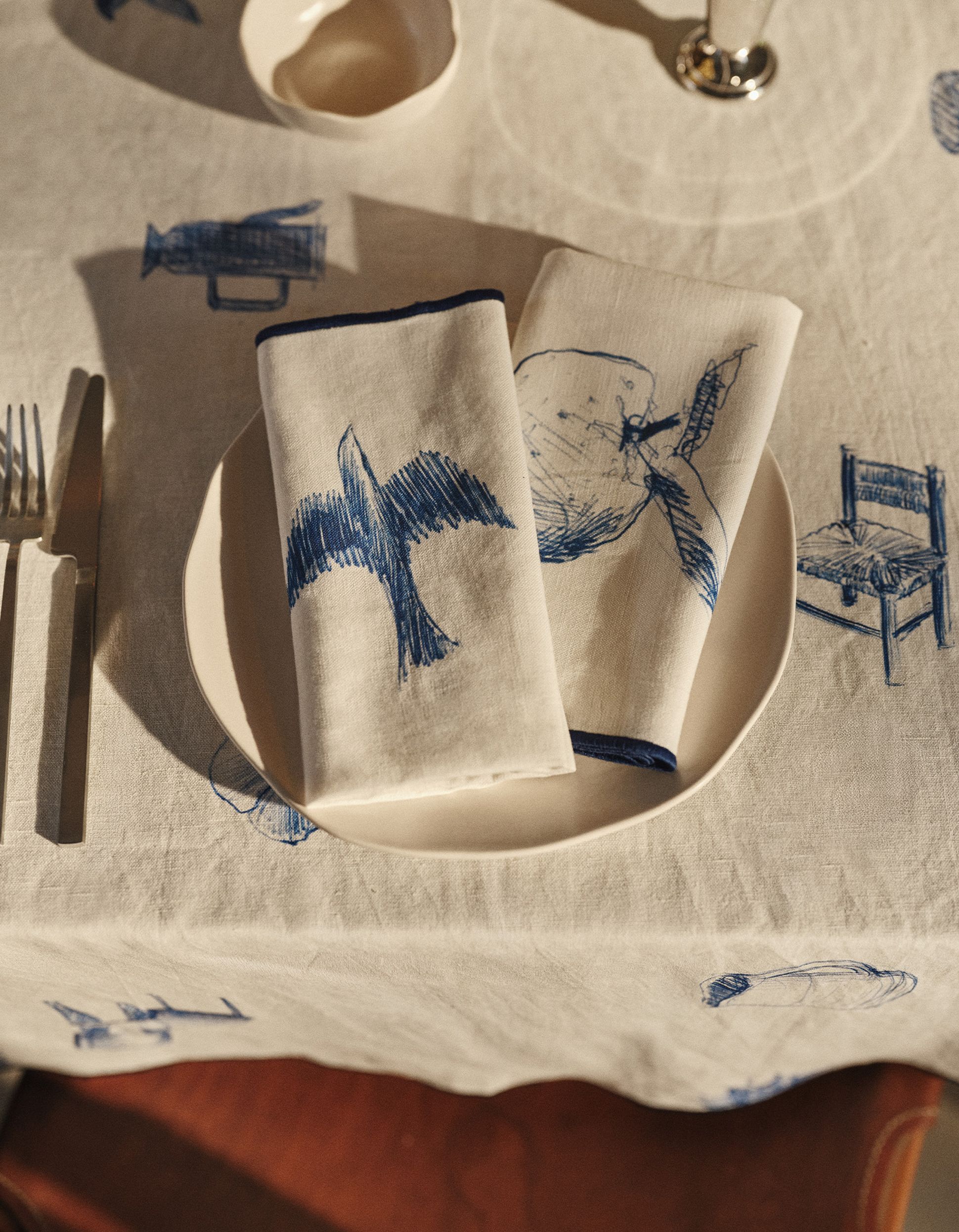 Une table dressée avec une assiette blanche sur laquelle reposent deux serviettes ornées de dessins d'animaux bleus, posée sur une nappe aux motifs similaire