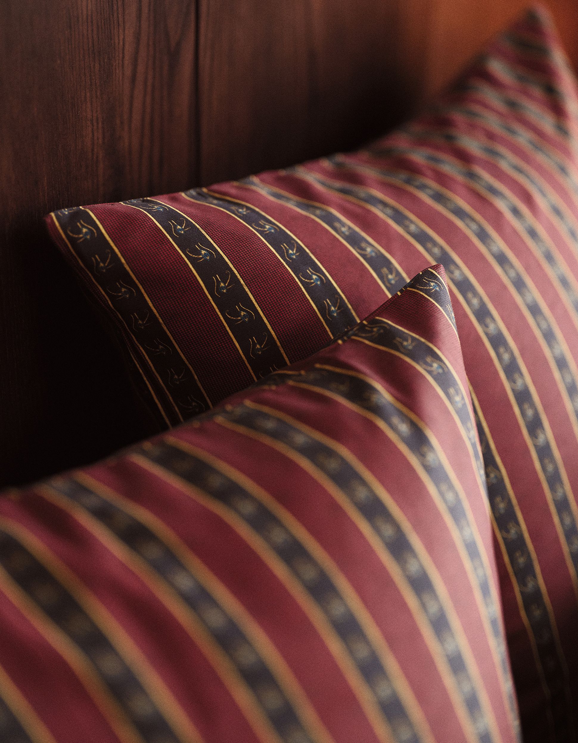 Two decorative pillows with maroon, gold, and navy striped patterns are placed against a dark wooden headboard.