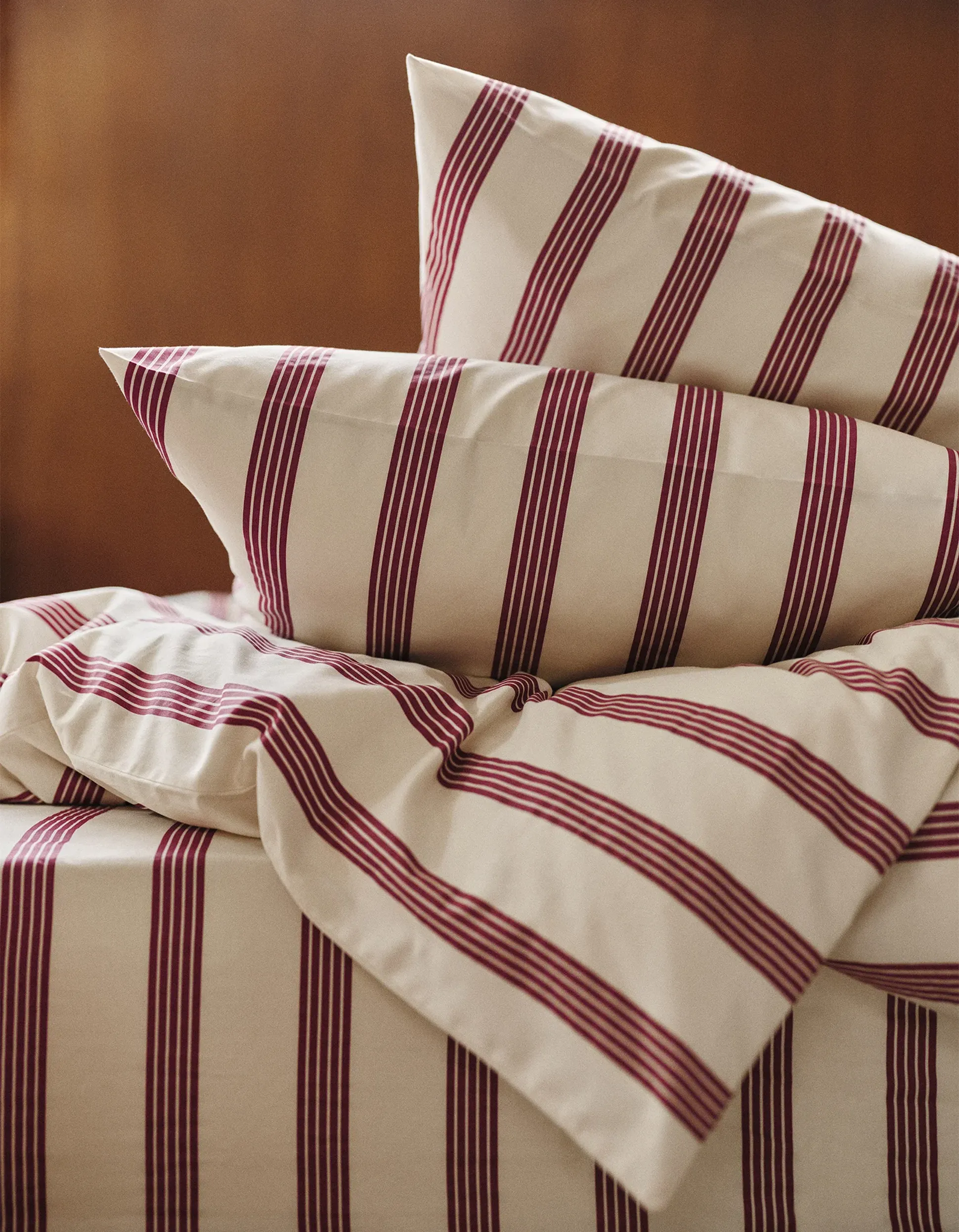 Un lit recouvert de draps couleur crème ornés de larges rayures verticales rouges, soigneusement arrangé avec deux oreillers assortis.