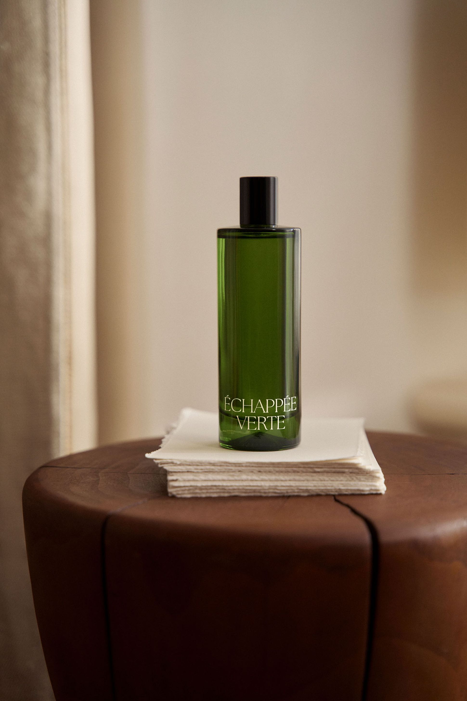 Un flacon de parfum vert portant l'inscription « ÉCHAPPÉE VERTE » posé sur une table en bois, sur un fond neutre et doux.