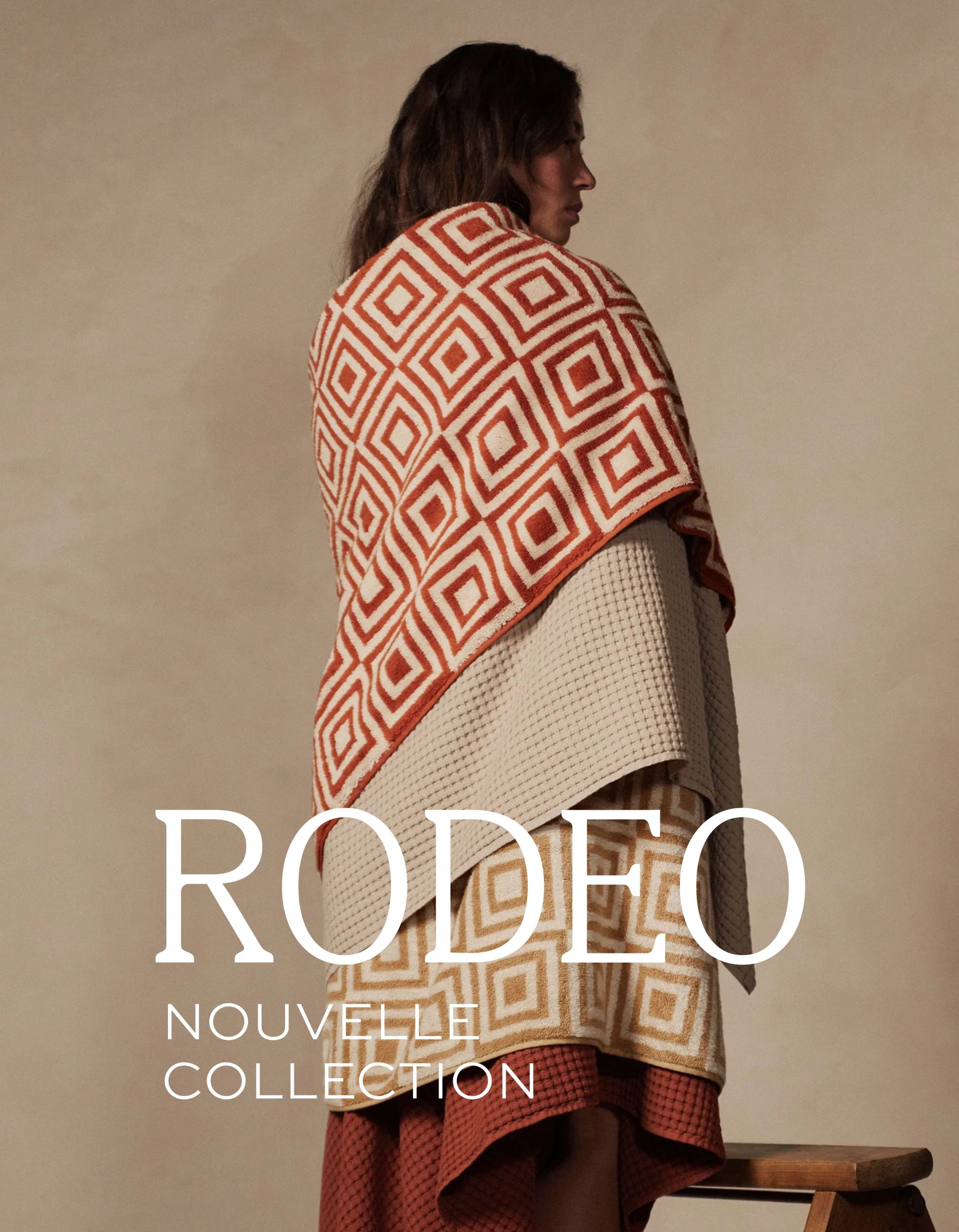 Une personne enveloppée dans des serviettes à motifs se tient debout sur une chaise devant un fond neutre. Le texte indique « RODEO NOUVELLE COLLECTION ».