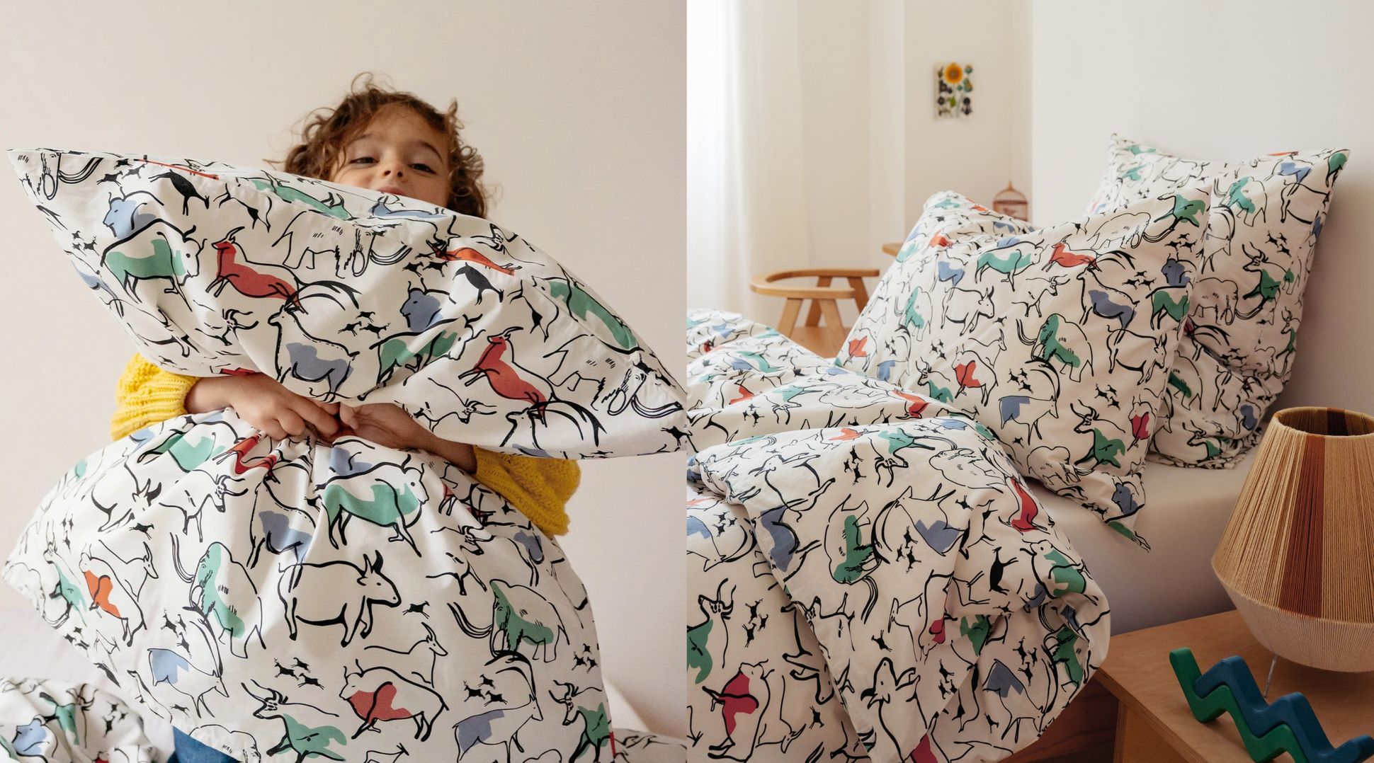 Enfant tenant des coussins à motifs animaliers à côté d'un lit recouvert de draps assortis, dans une pièce lumineuse à la décoration simple.