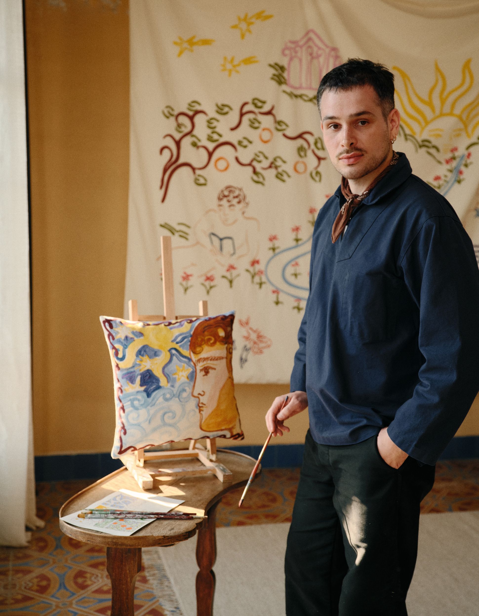 L'artiste Jacques Merle, un pinceau à la main qui travaille sur un tableau qui sera ensuite un coussin issu de la collaboration entre Jacques Merle et Bonsoirs
