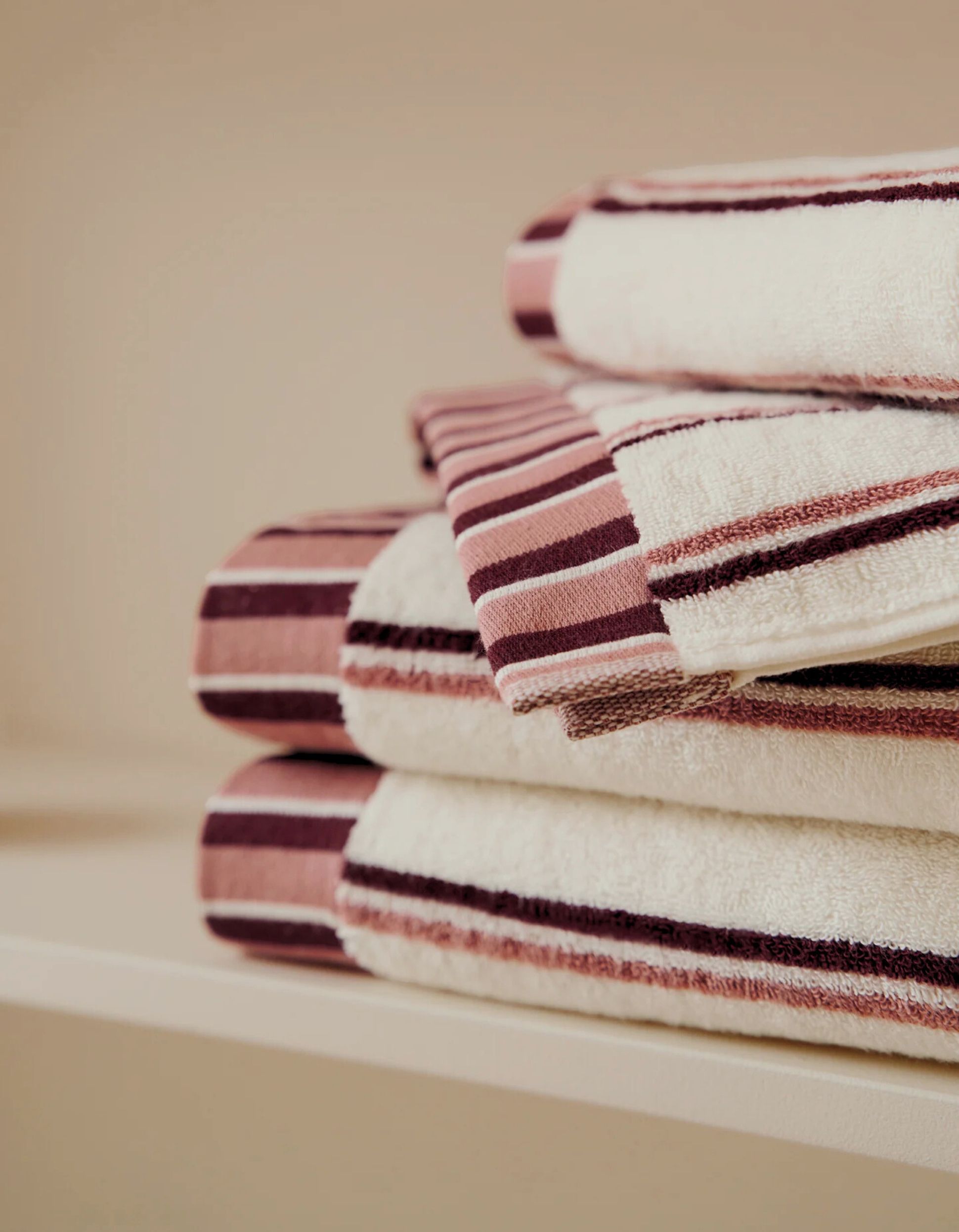 Pile de serviettes soigneusement pliées, rayées marron et rose, posées sur une étagère.