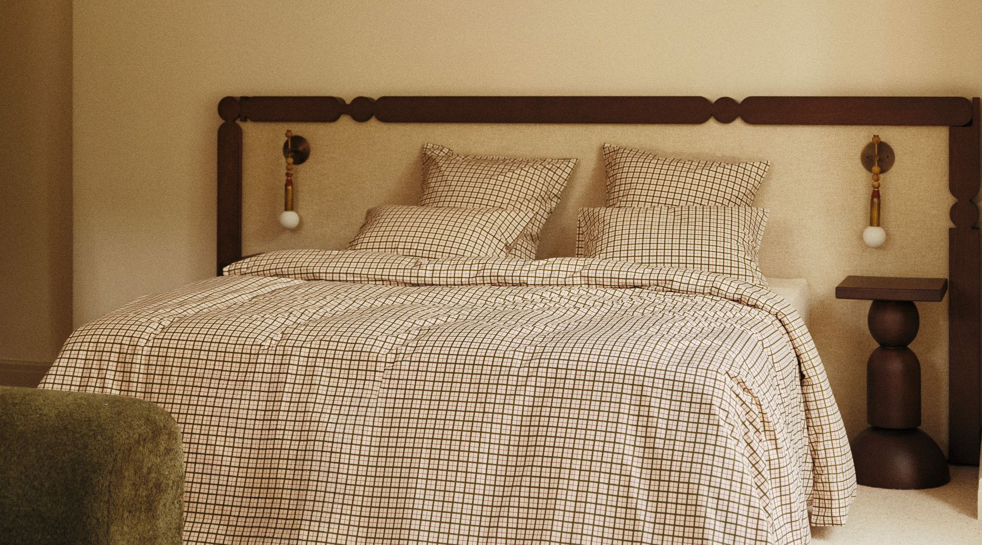 Une chambre moderne avec un lit orné d'une parure de lit à carreaux, d'une tête de lit en bois, de lampes murales et d'une table de chevet en bois.