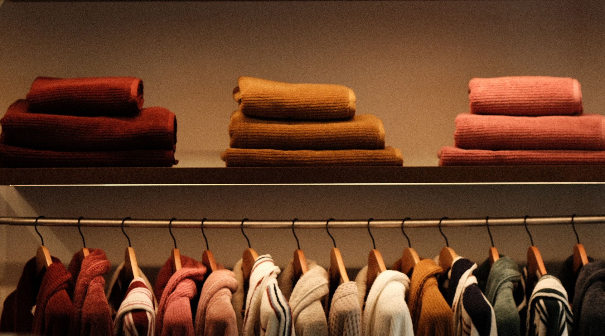 Une rangée de peignoirs rouges et roses suspendus à des cintres en bois, avec des serviettes pliées empilées sur une étagère au-dessus.