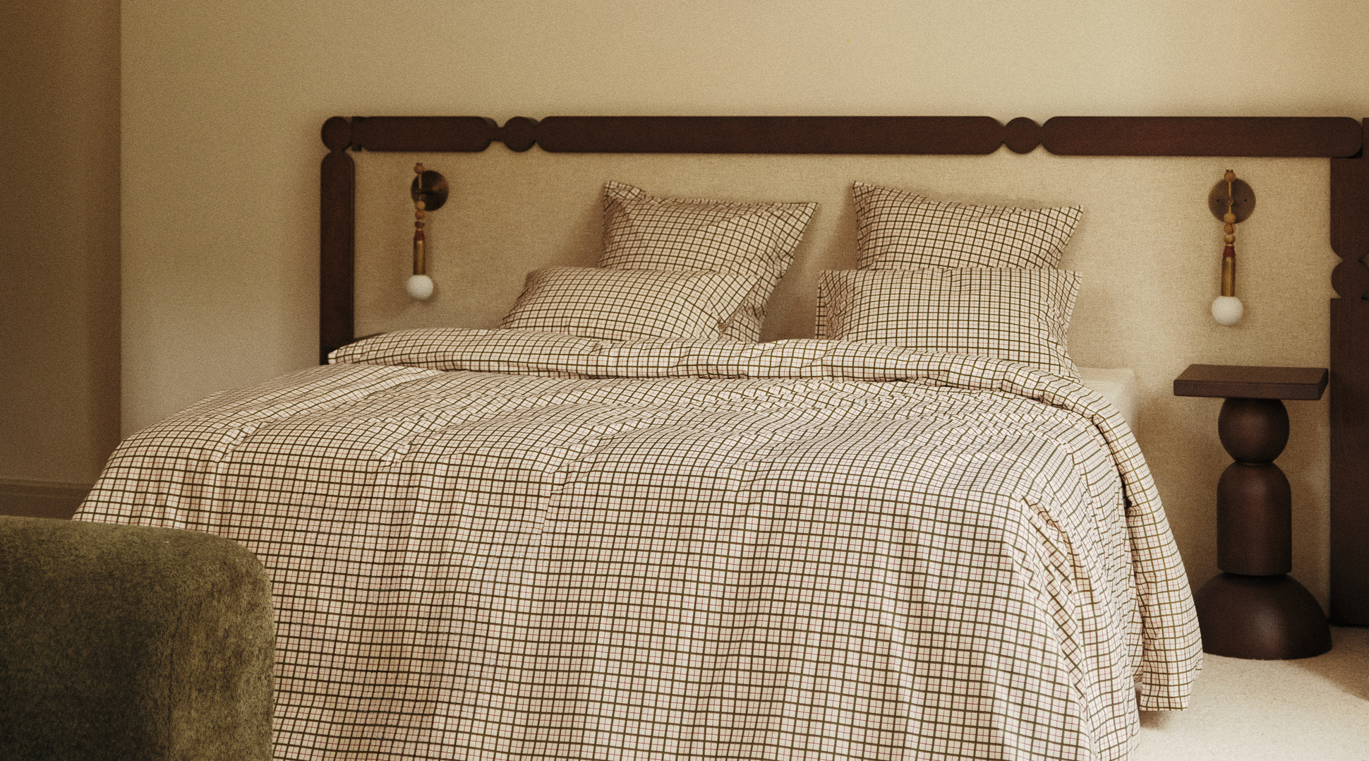 Un lit soigneusement fait, avec une parure à carreaux, une tête de lit en bois et des tables de chevet assorties, dans une chambre à la lumière tamisée.
