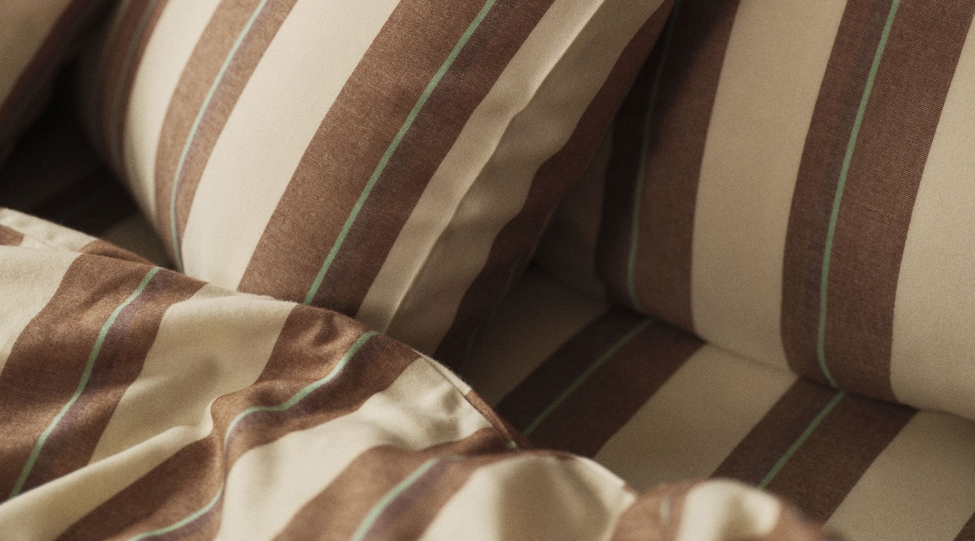Gros plan sur un lit orné d'oreillers et d'une couverture rayés de marron et de beige, devant une tête de lit en bois foncé.