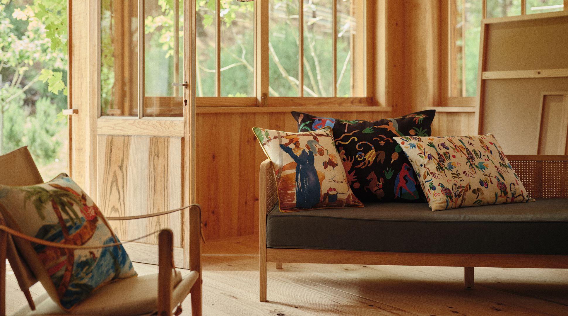 Une chambre chaleureuse en bois, avec un canapé, des coussins aux motifs colorés et une lanterne en papier aux couleurs vives près de la fenêtre.