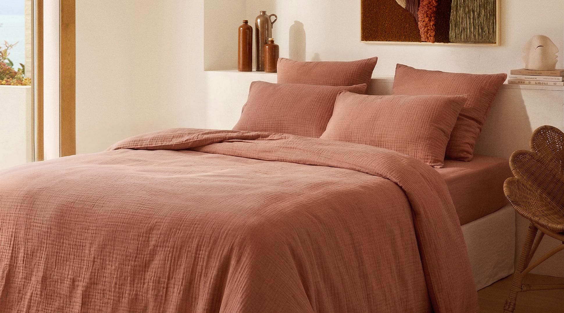 Une chambre douillette avec un lit recouvert de draps doux couleur rose, dans un décor rustique baigné d'une lumière naturelle et chaleureuse.