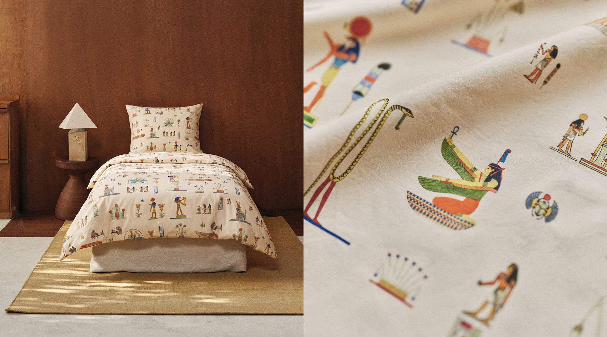 Un ensemble de literie beige orné de motifs égyptiens, notamment des personnages et des symboles, posé sur un lit en bois accompagné d'une table de chevet et d'une lampe. Gros plan sur un détail du motif.