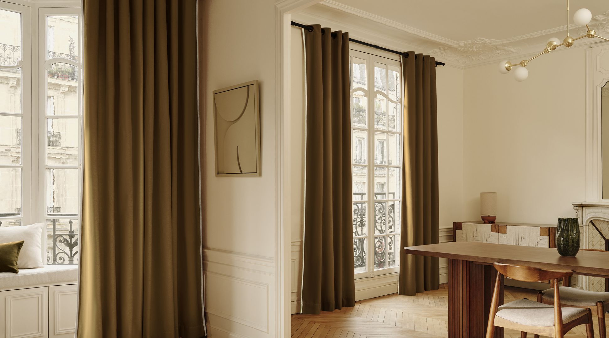 Une pièce élégante dotée de grandes fenêtres ornées de rideaux marron, d'une table et d'une chaise en bois, d'un lustre moderne et d'une décoration minimaliste.