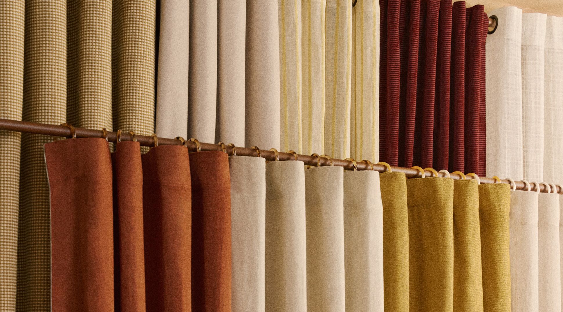 Une variété de rideaux en tissu rouge, beige, jaune et à motifs sont suspendus à une tringle dans la vitrine d'un magasin.