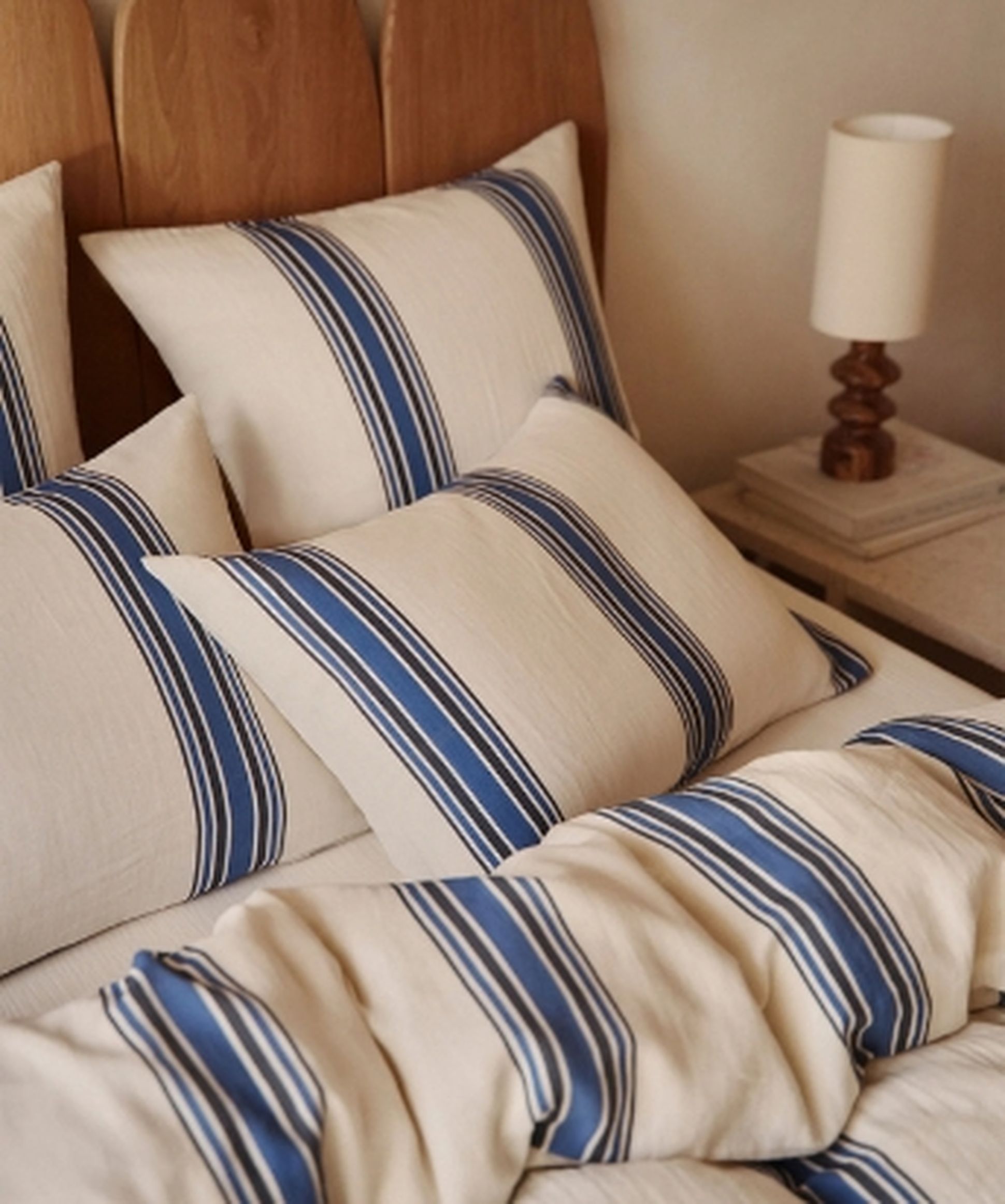 Un lit avec des oreillers et une couverture à rayures bleues, une tête de lit en bois et une table de chevet avec une lampe.