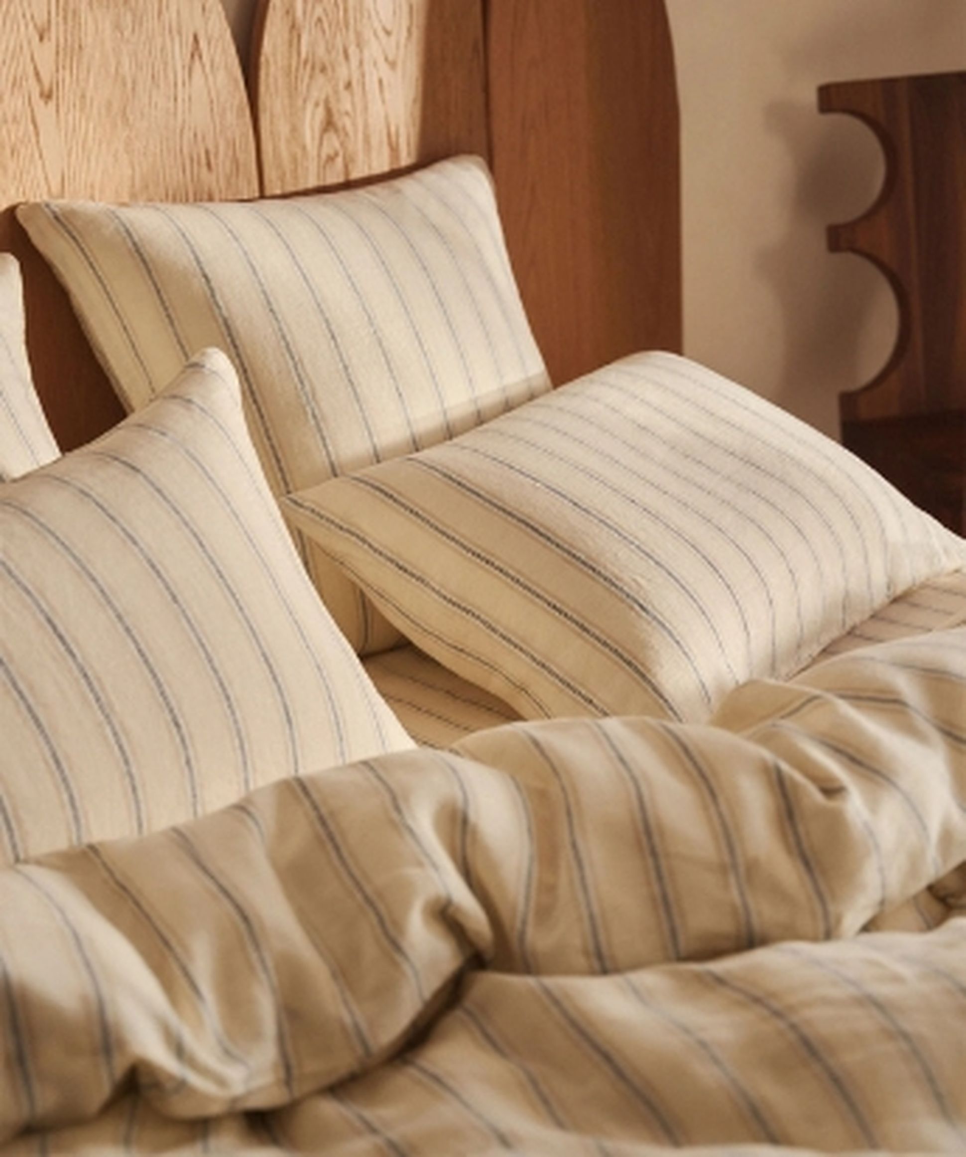 Une chambre douillette avec un lit bien fait, une parure de lit rayée et des oreillers moelleux près de la fenêtre. Sur la table de chevet se trouvent un livre et une lampe.